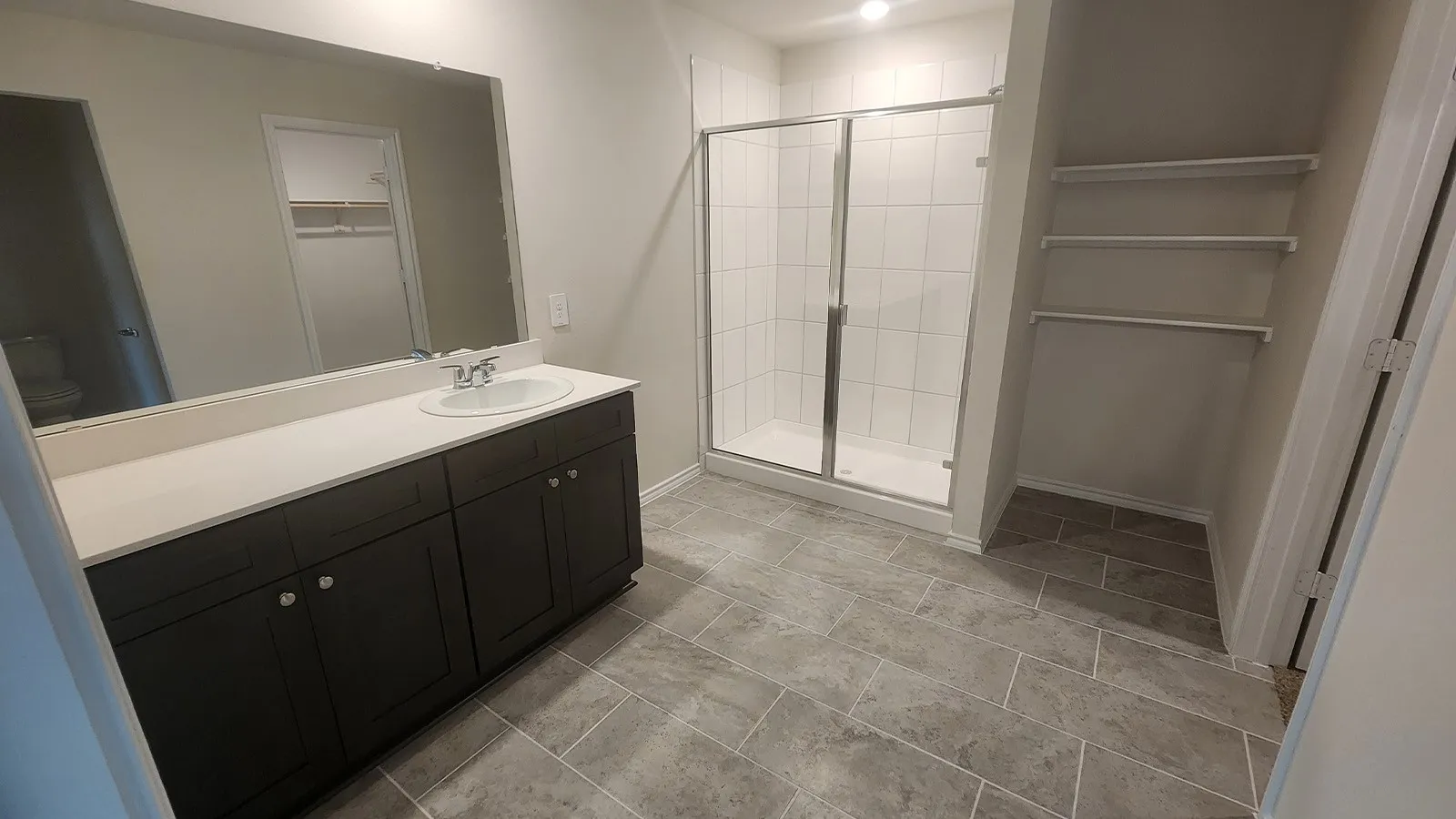 Vanity with an integrated sink, expansive mirror, glass-enclosed shower, built-in shelving, and tile flooring