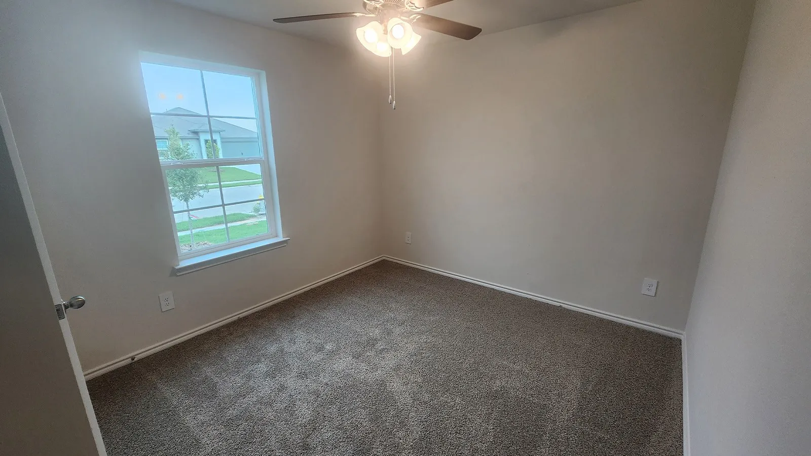 Neutral wall color, carpeted flooring, window with white trim, and a ceiling fan with integrated lighting