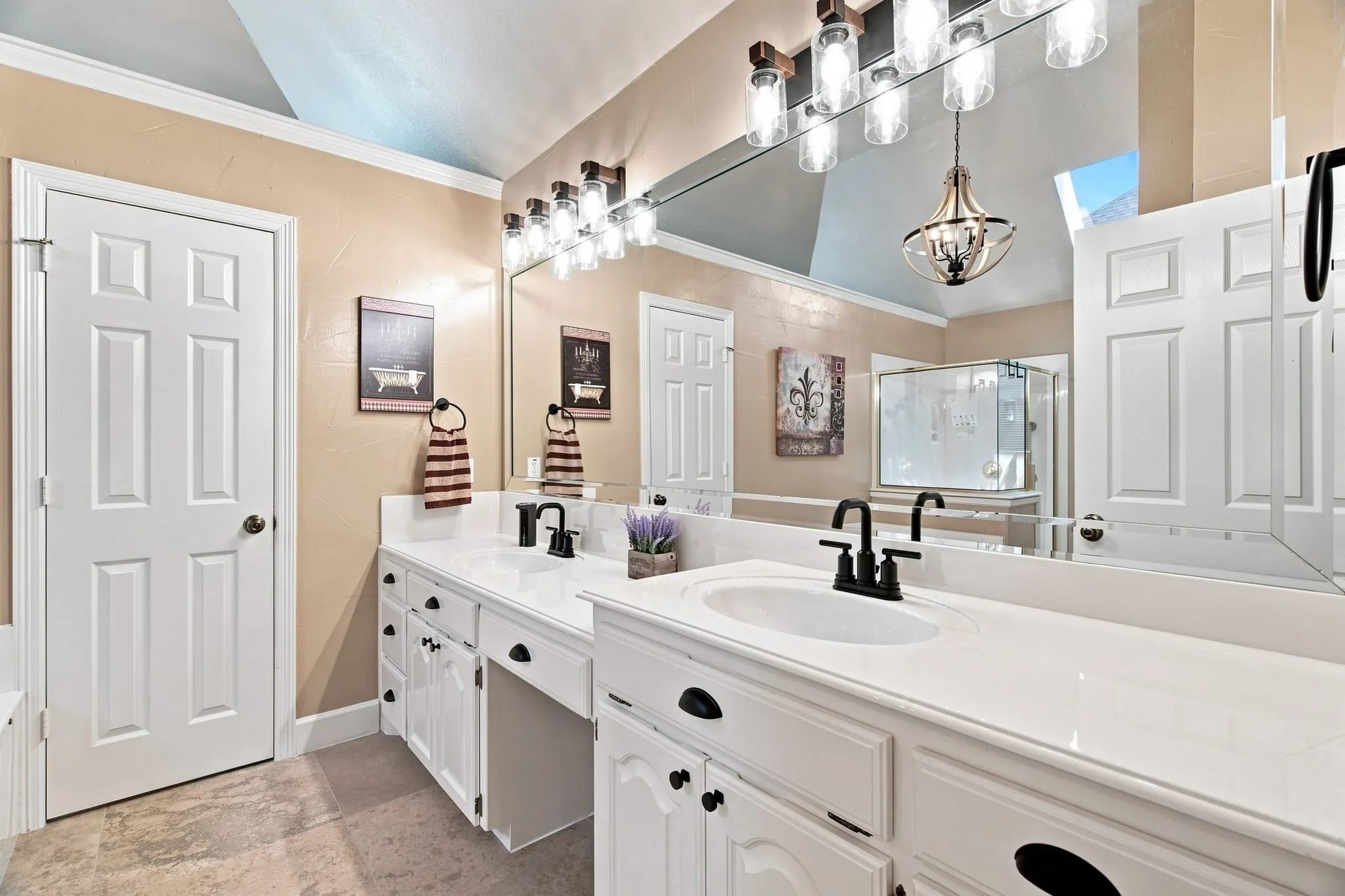 Spa-inspired primary bathroom featuring dual vanities with white cabinetry, white quartz countertops, and matte black hardware
