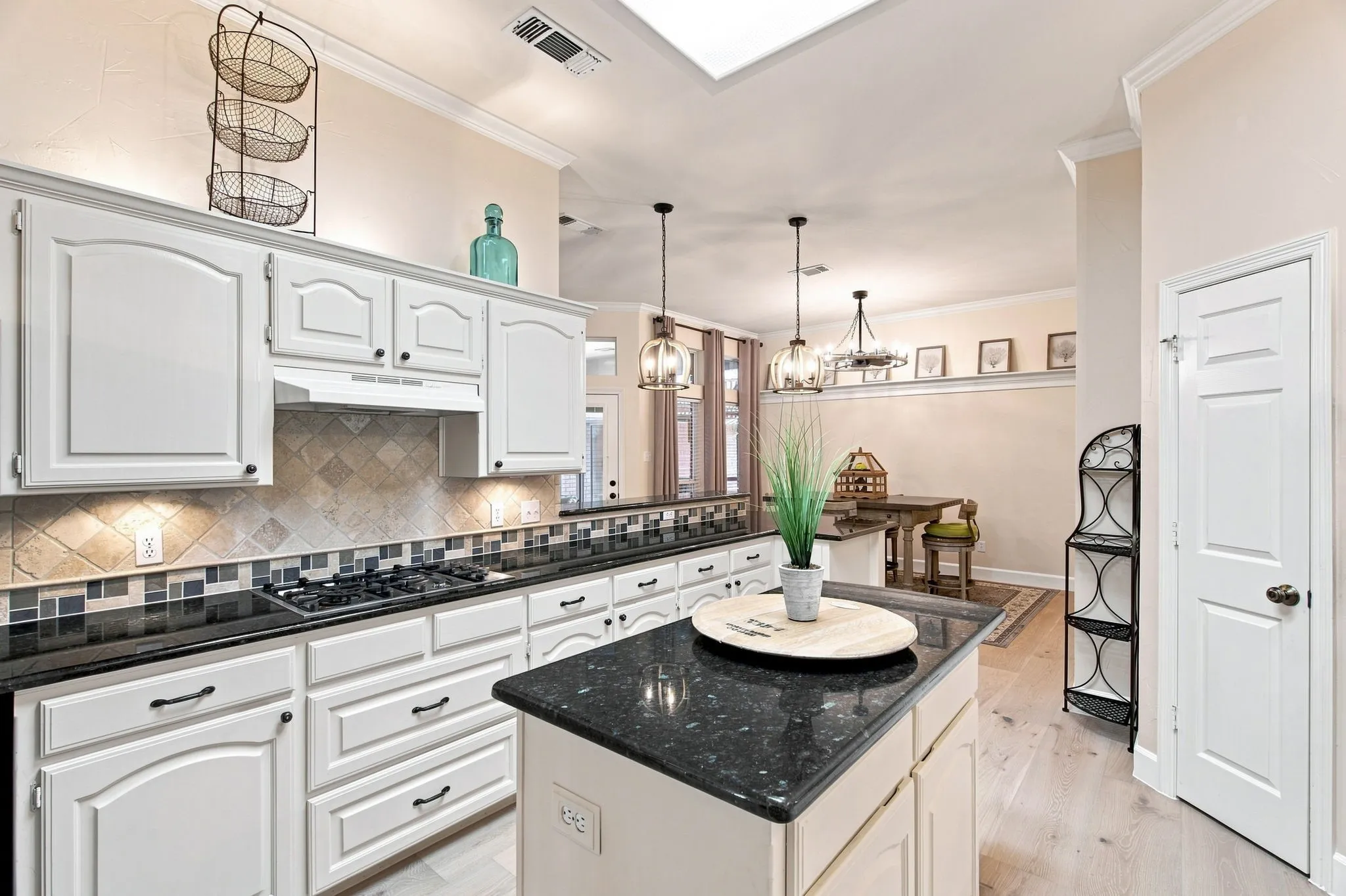 White cabinetry with black hardware, black stone countertops, tile backsplash, built-in gas range, and wood-finish flooring