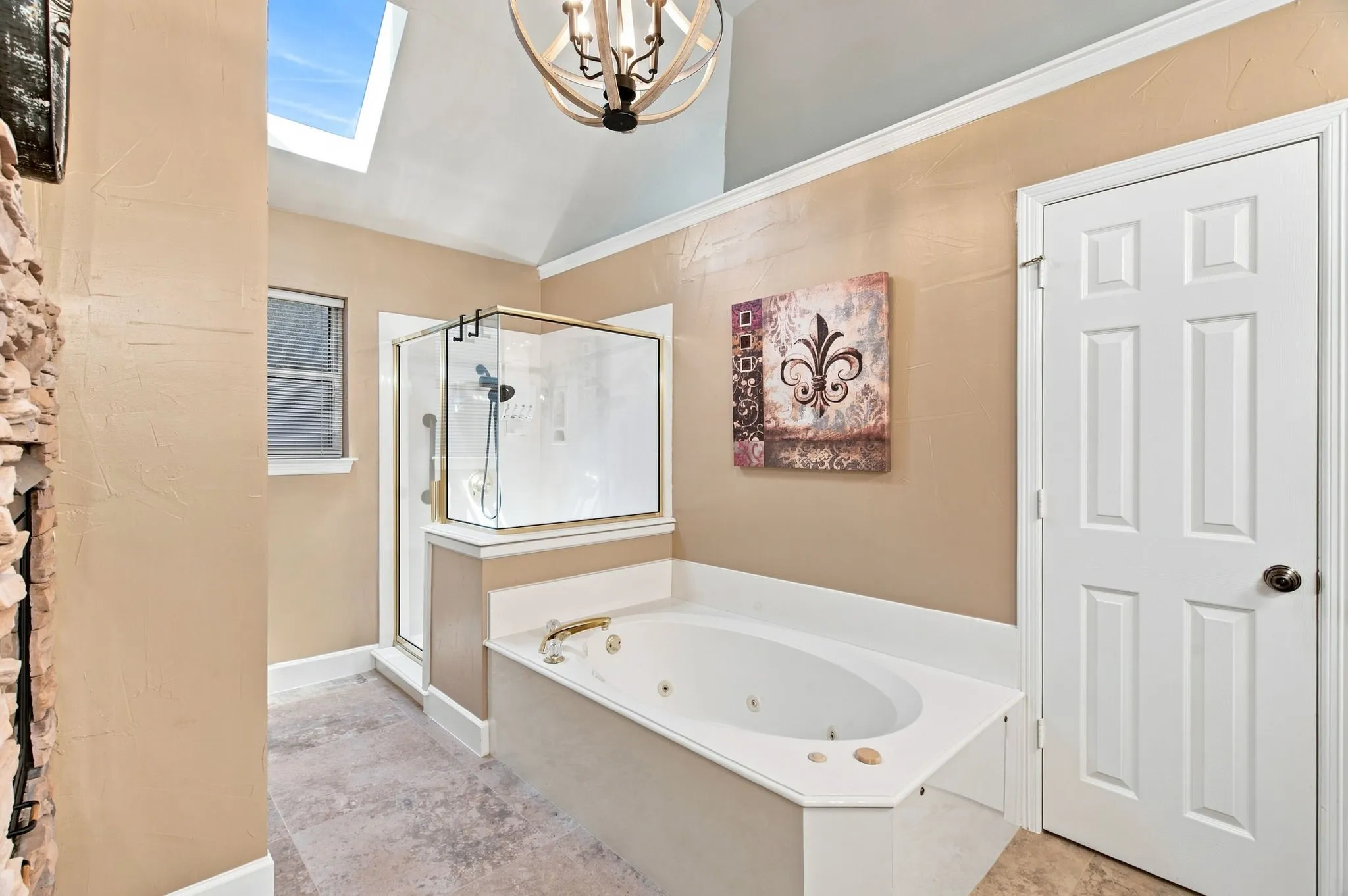 Spa-inspired primary bathroom featuring a freestanding soaking tub, a frameless glass-enclosed walk-in shower with dual showerheads, neutral tile flooring, soft peach wall finishes, skylights for natural illumination, and decorative wall art