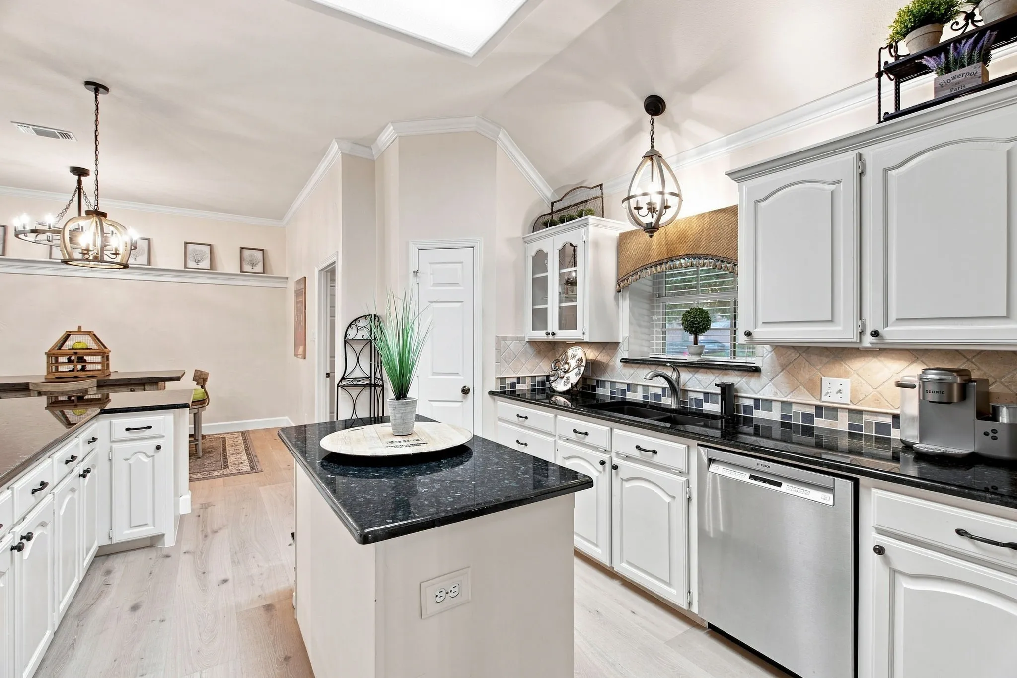 Kitchen featuring white cabinetry, dark countertops, a central island, a tile backsplash, and light wood-finish flooring