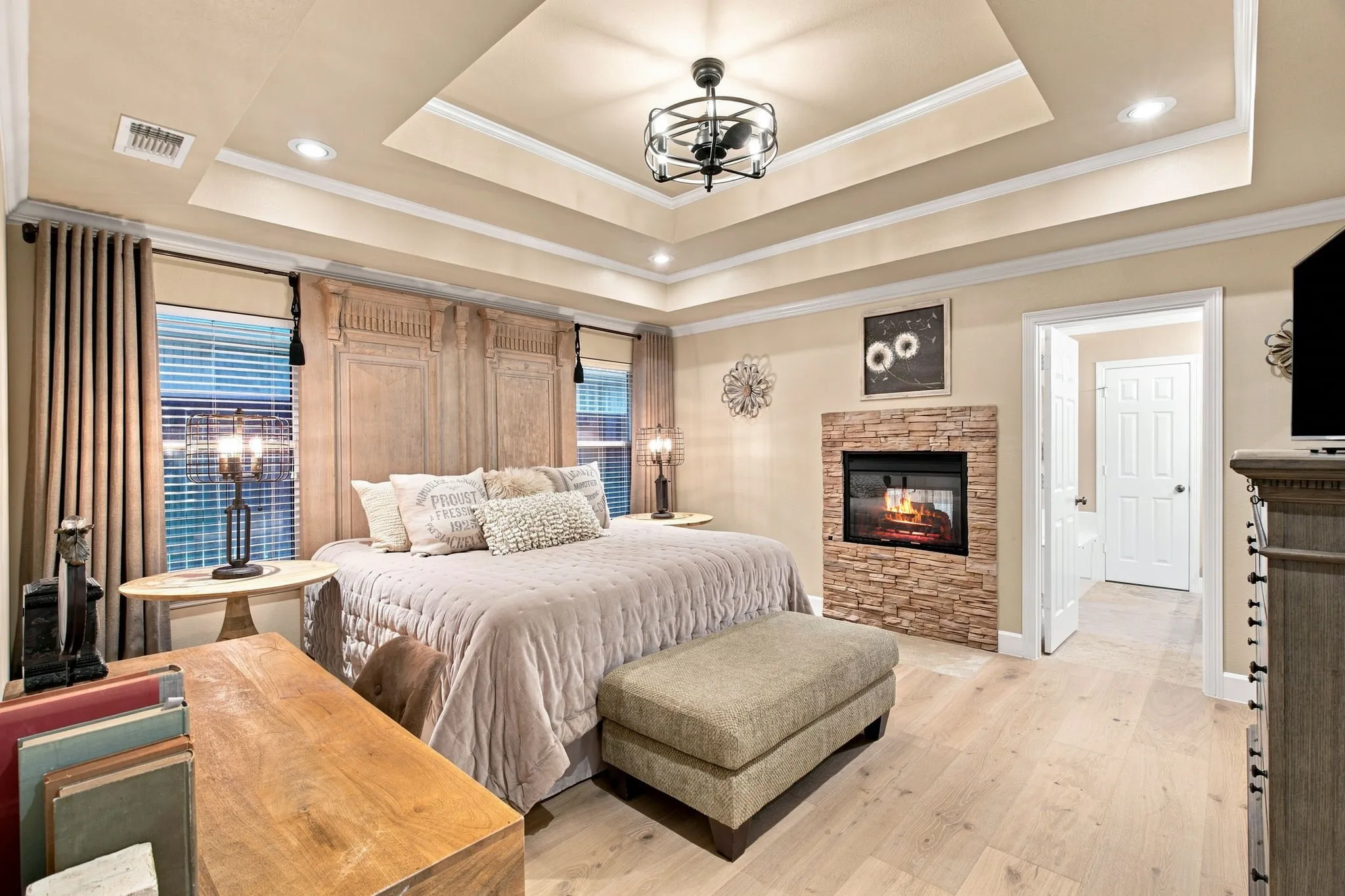 Tray ceiling with recessed lighting and crown molding, wood-finish flooring, built-in electric fireplace with stacked stone surround, and decorative wall paneling