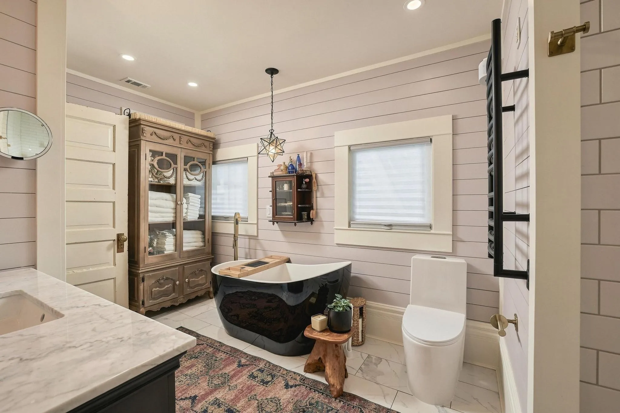 Showstopper! This bath combines eras beautifully with a black freestanding soaking tub, shiplap walls and large format floor tile.