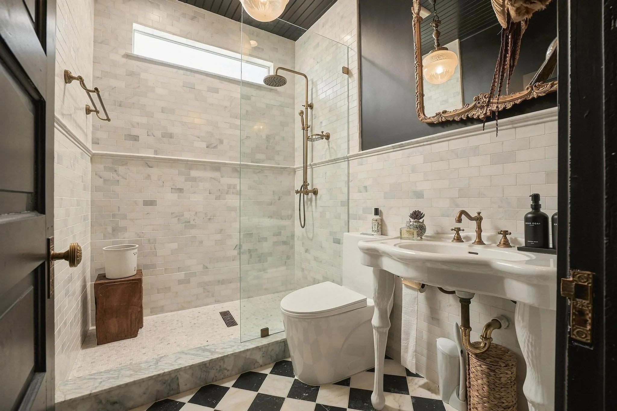 The main level bath has spectacular patterned marble floors, frameless glass shower panel, graceful pedestal sink and gilded statement mirror.