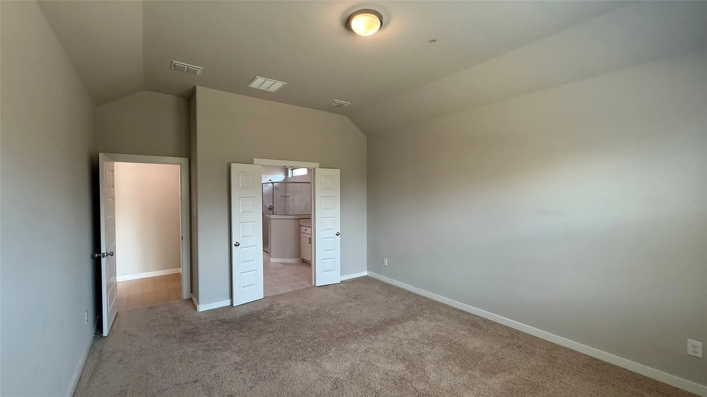 Spacious room featuring vaulted ceilings, neutral-toned carpeting, and a flush-mount ceiling light
