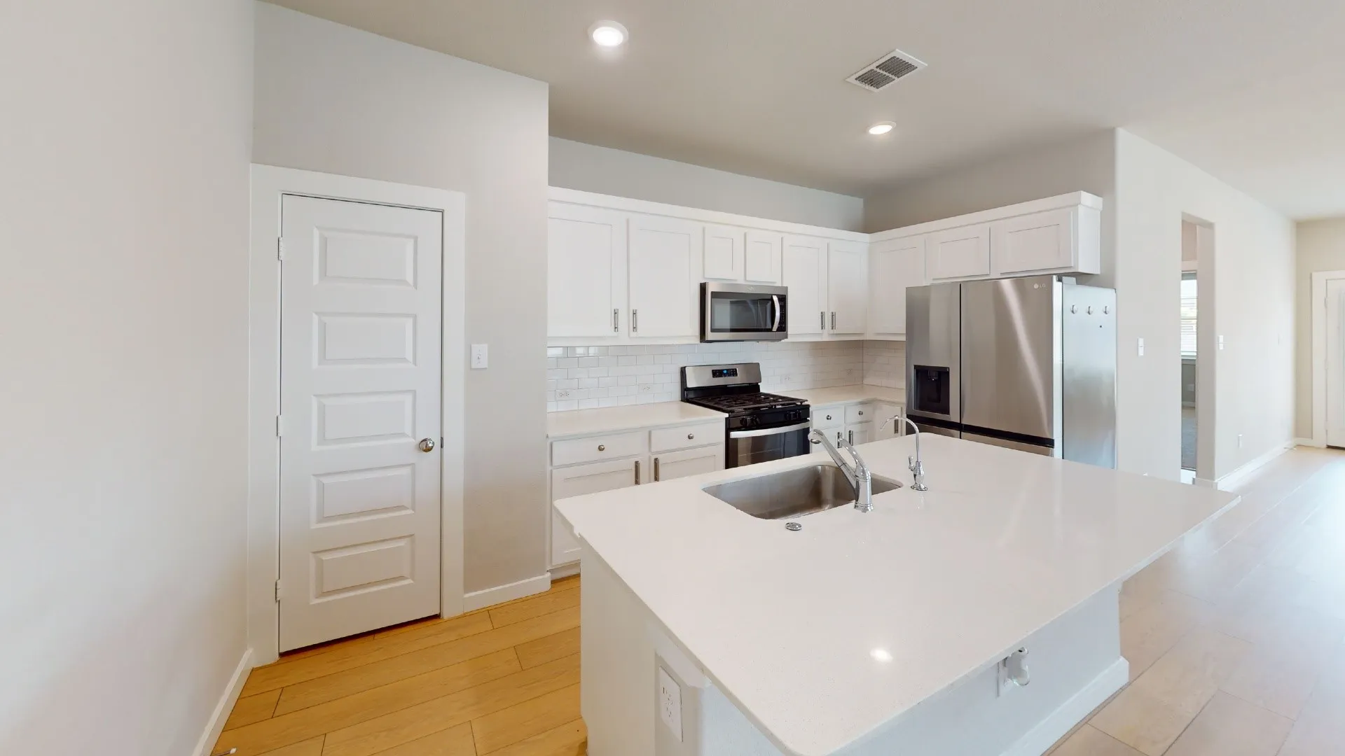 Modern kitchen featuring white cabinetry, stainless steel appliances, a white subway tile backsplash, and a large island with an integrated sink