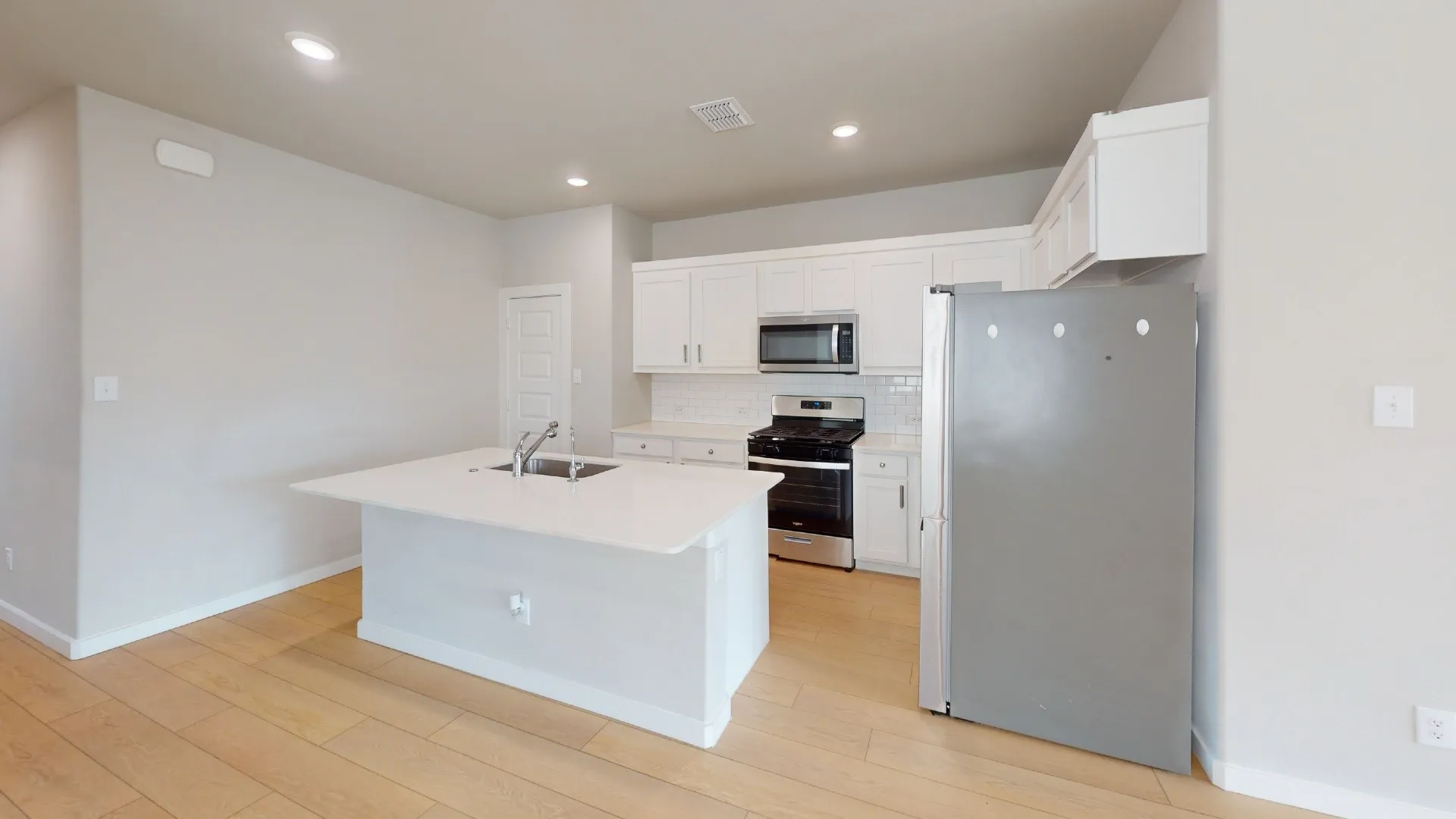 Kitchen featuring a central island with an undermount sink, white cabinetry, stainless steel appliances, and wood-finish flooring