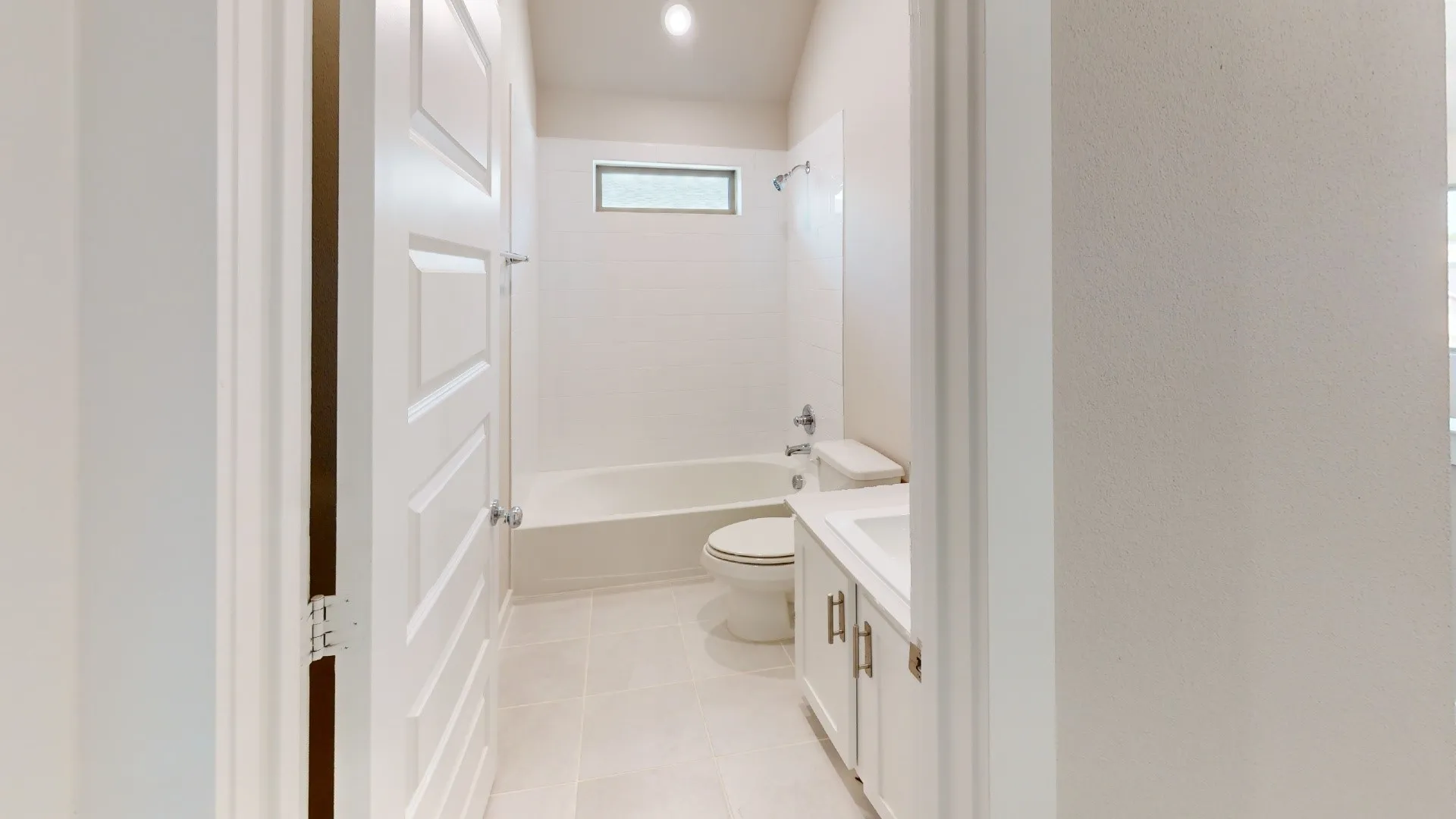 White panel door opening to a bathroom with a tub/shower combination, white vanity, and rectangular transom window