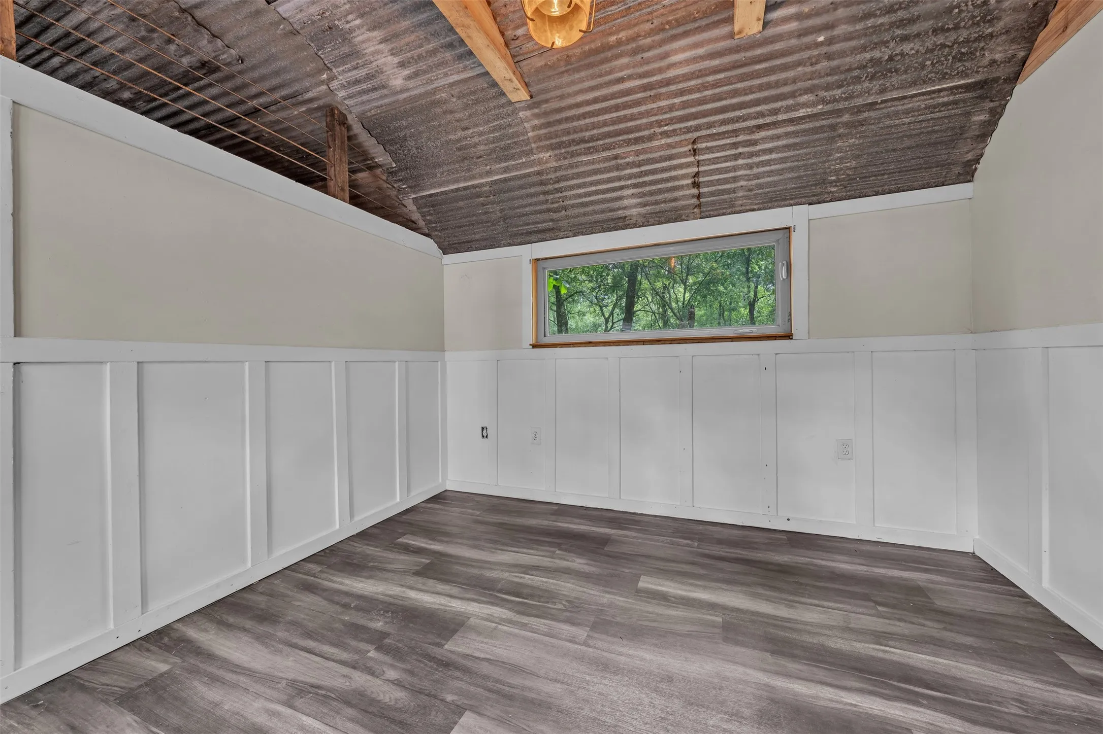 Corrugated metal ceiling, board and batten wainscoting, wood-finish flooring, recessed window, and exposed wood beam