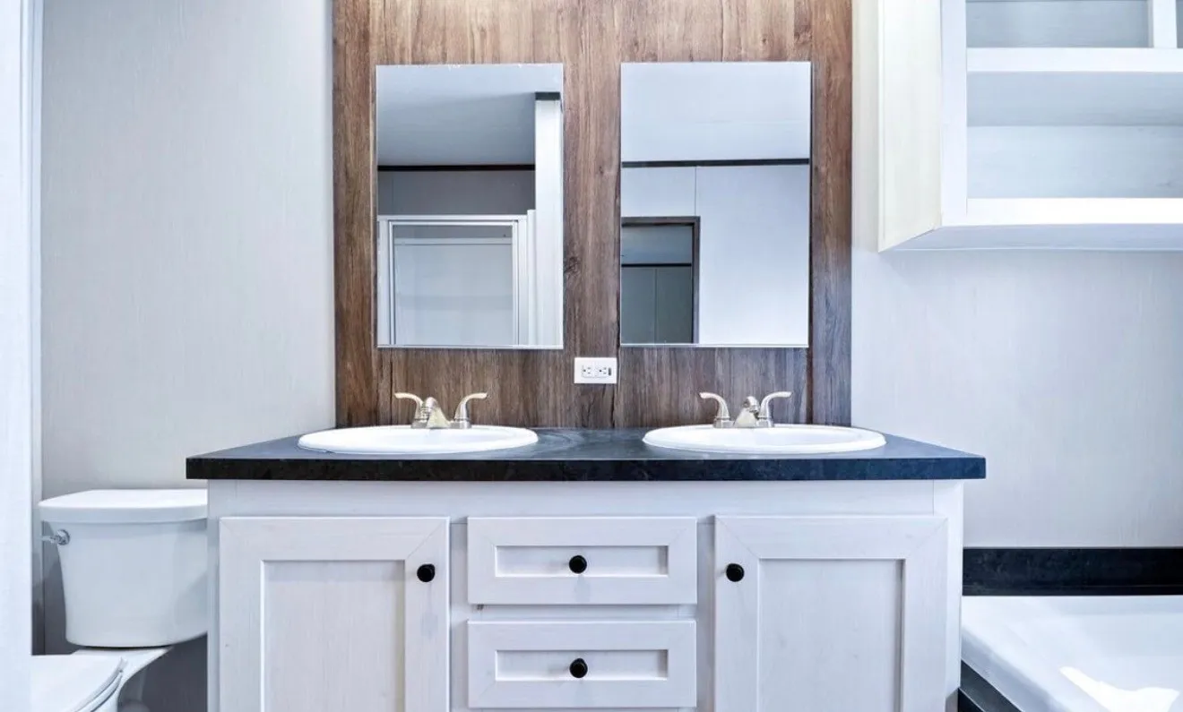 Dual vanity with white cabinetry, black hardware, black countertop, two undermount sinks, and wood-finish accent wall with two mounted mirrors