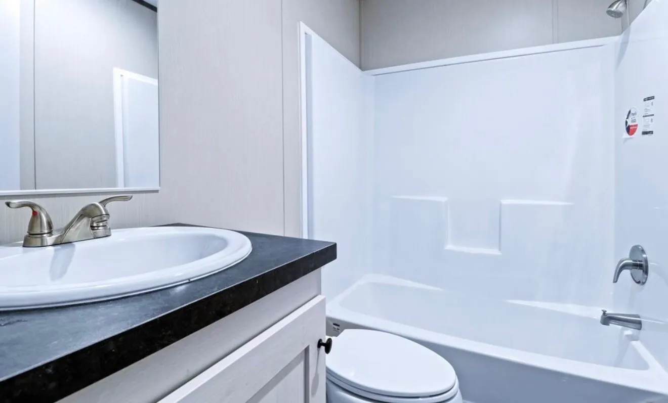 Vanity with a dark countertop and undermount sink, brushed nickel faucet, and a white bathtub and shower surround