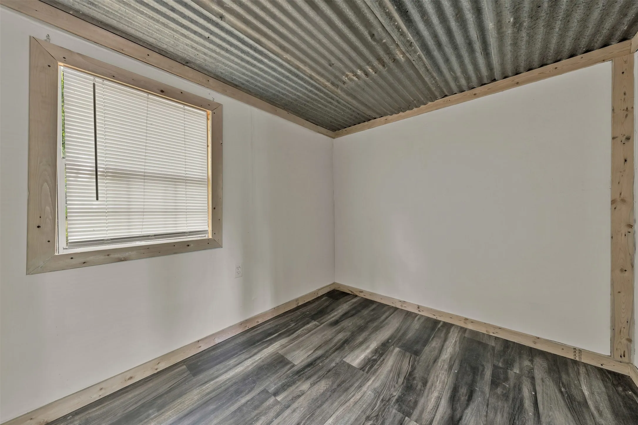 Corrugated metal ceiling, wood-finish flooring, white walls, and a window with blinds