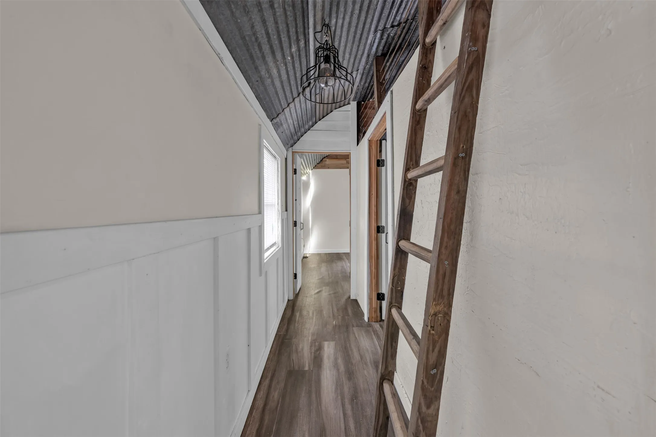 Corrugated metal ceiling, plank wall paneling, wood-finish flooring, and a window
