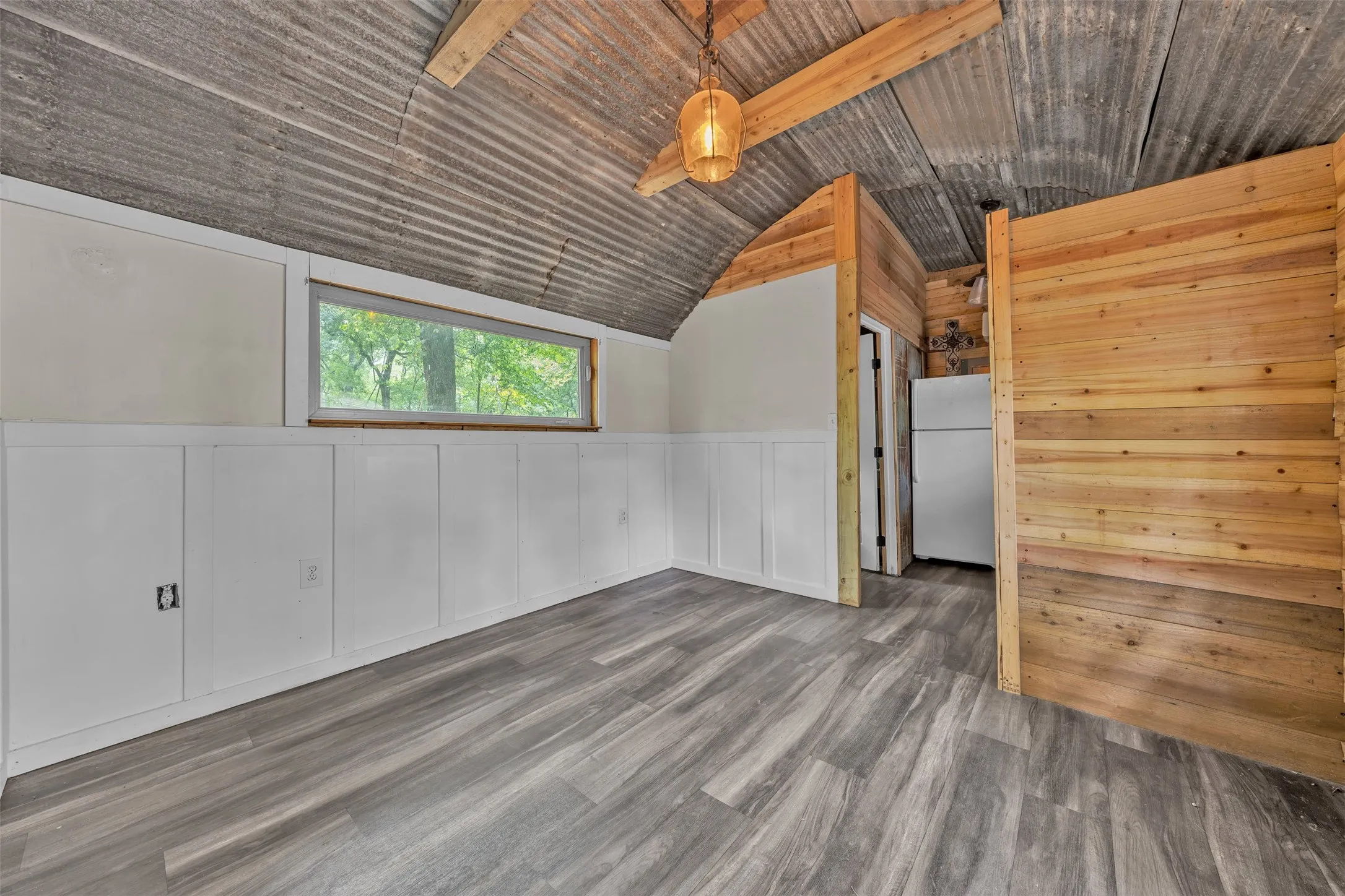 Corrugated metal ceiling, exposed wood beams, window, wood-finish flooring, built-in storage