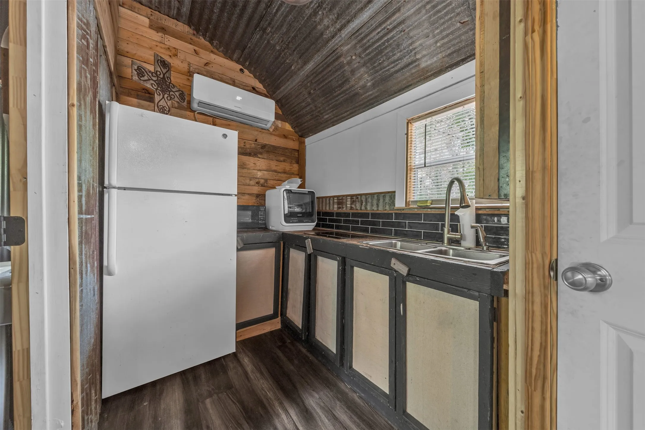 Wood-paneled wall, corrugated metal ceiling, wood-finish flooring, built-in cabinetry, and a double basin sink with a high-arc faucet