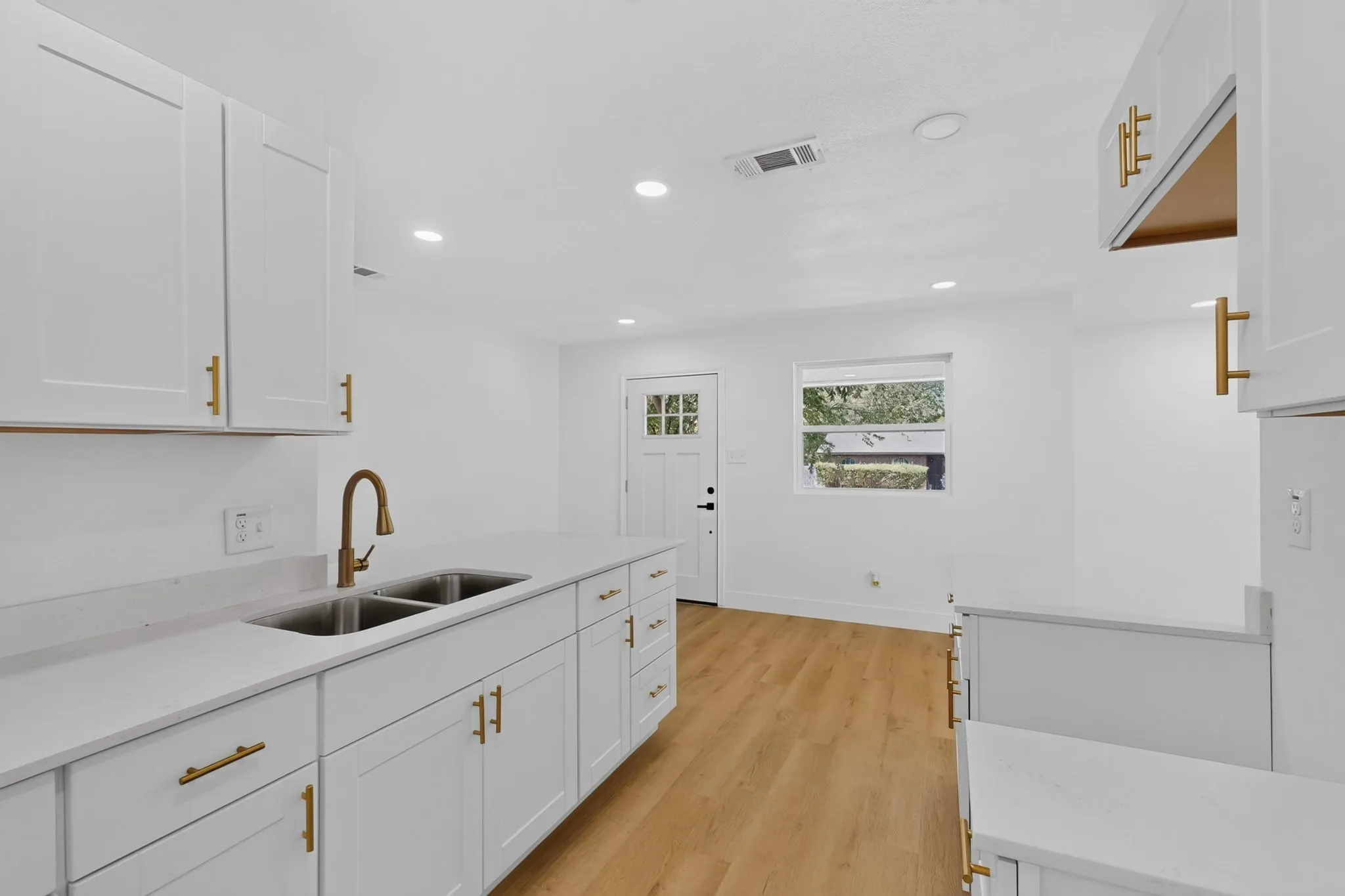 White shaker-style cabinetry with gold-finish hardware, light-toned countertops, and a dual basin sink with a gooseneck faucet