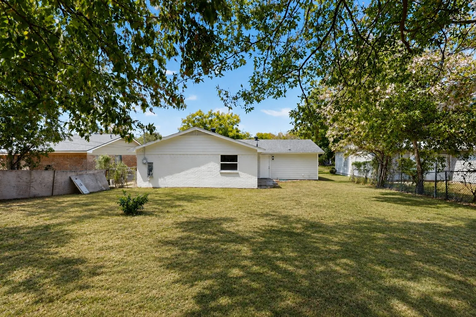 Expansive backyard with a lush lawn, mature trees, and a white stucco exterior