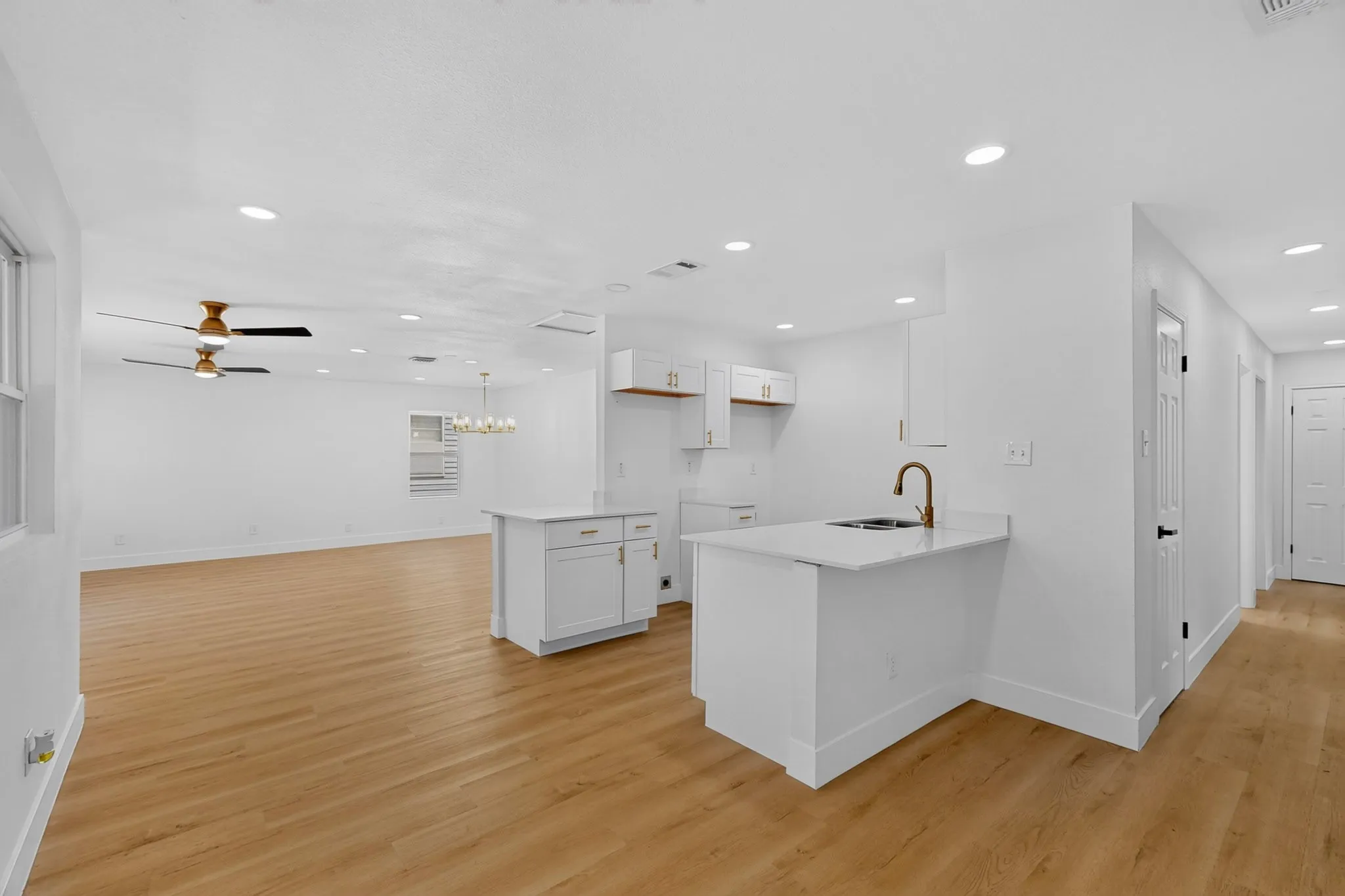 Open-concept living space featuring wood-finish flooring, recessed lighting, white cabinetry, and a kitchen island with a single-basin sink and a bronze-finish faucet