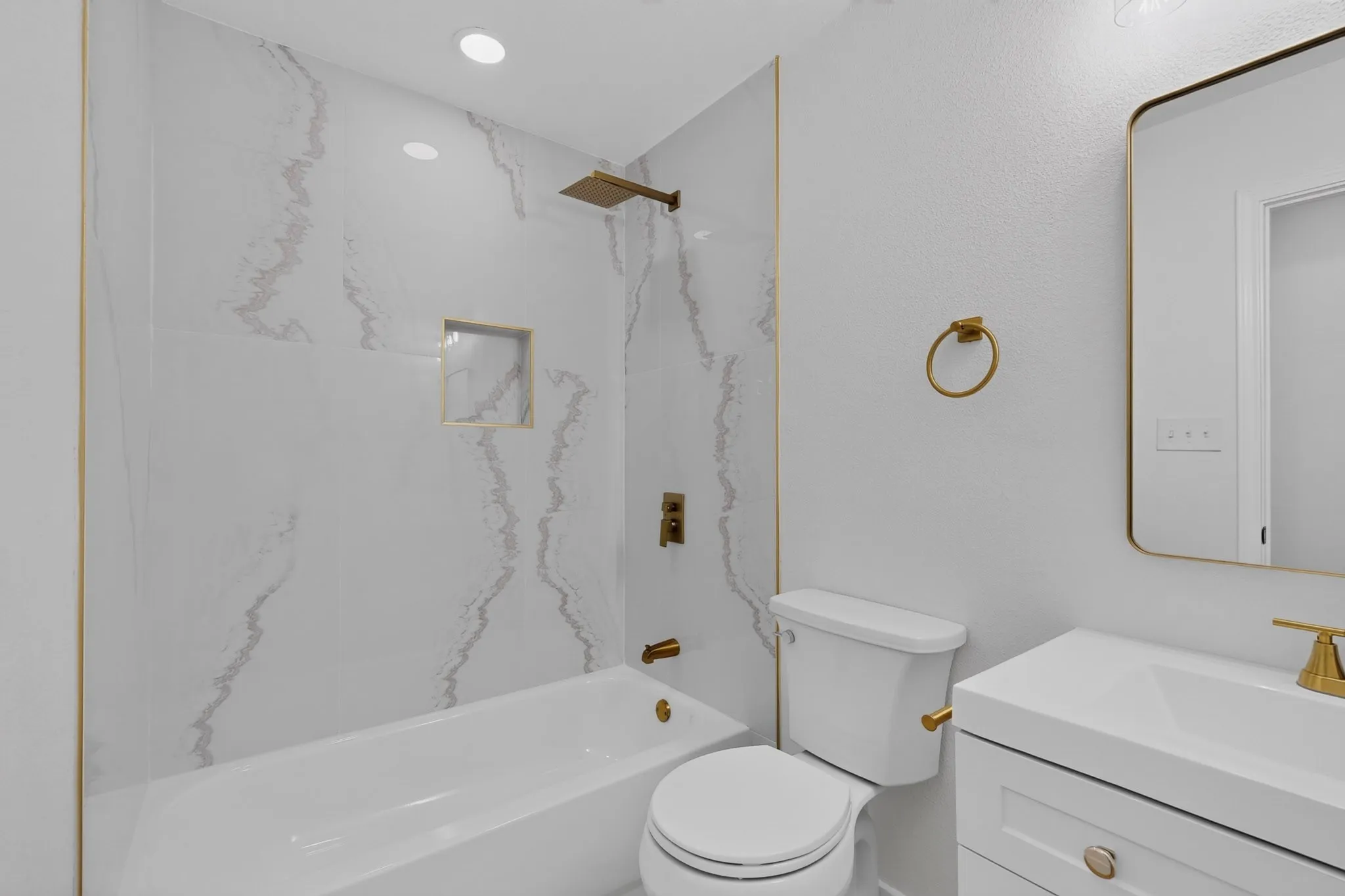 Modern bathroom featuring a white vanity with integrated sink, gold-tone fixtures, and a rectangular mirror