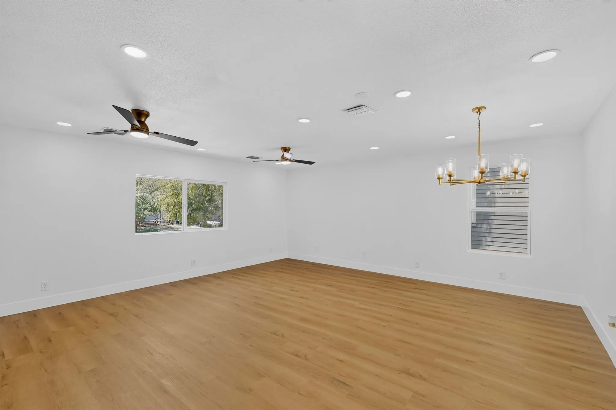 Spacious room featuring wood-finish flooring, recessed lighting, multiple ceiling fans, and a modern chandelier