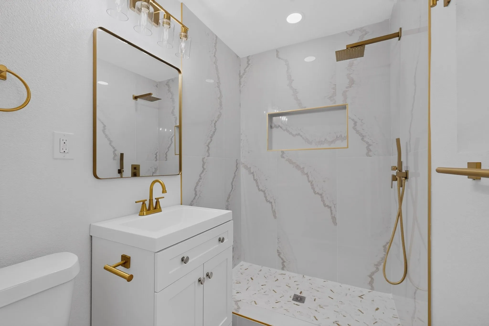 Bathroom featuring a white vanity with gold-finish hardware, rectangular mirror, and a walk-in shower with a mosaic tile floor and a recessed niche