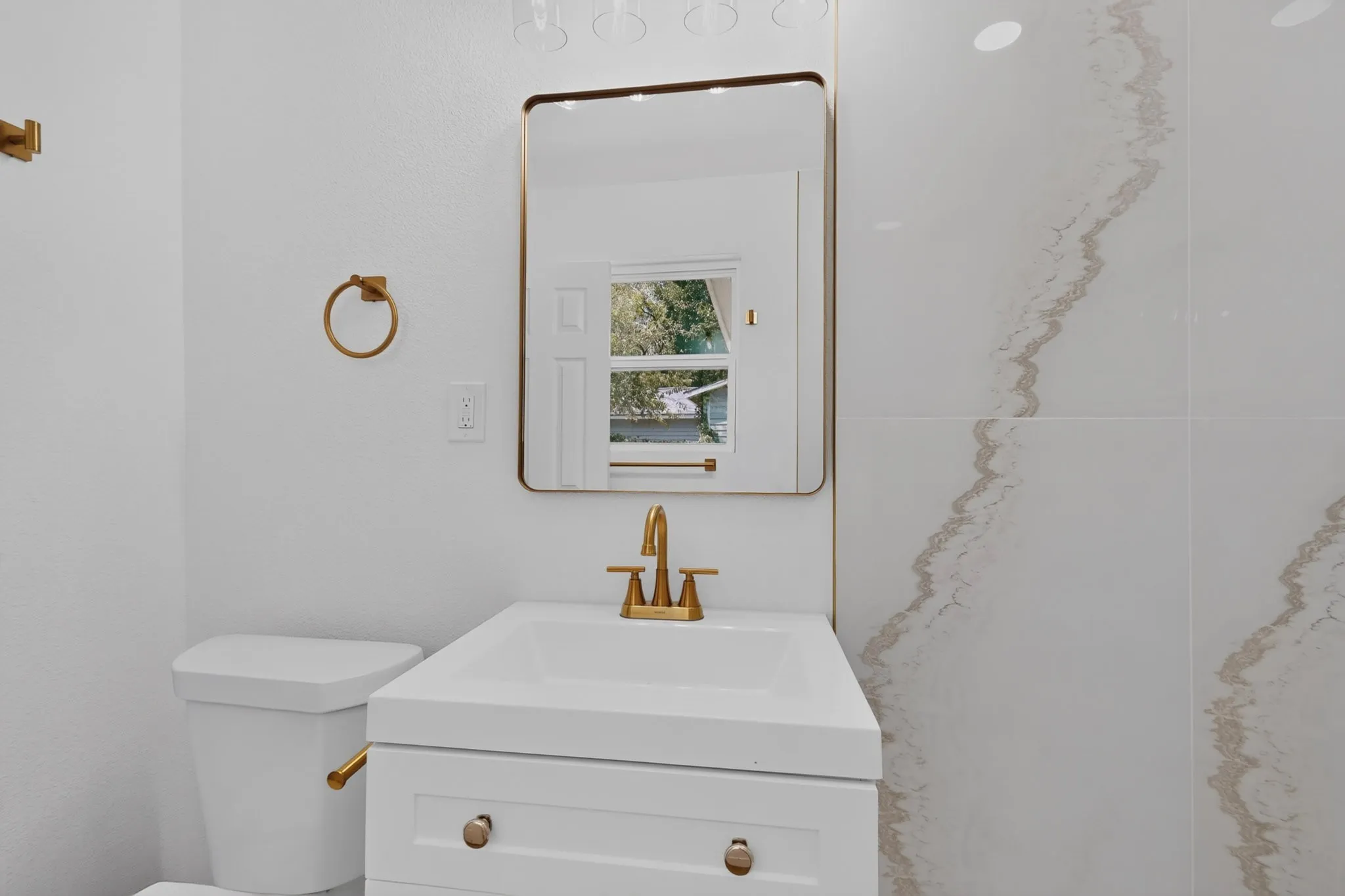 White vanity with integrated sink, brass-finish faucet, framed mirror, and vertical wall tiling
