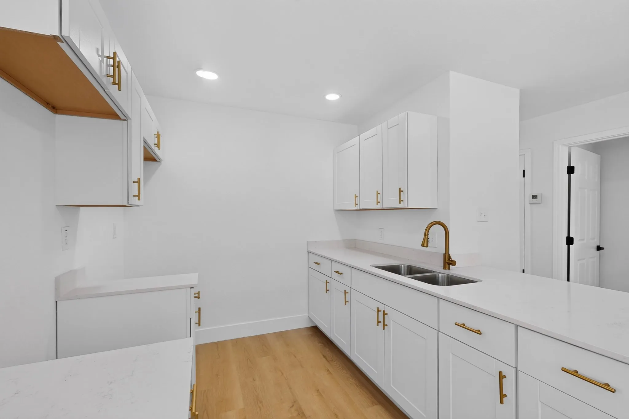 White shaker cabinetry with gold-tone hardware, wood-finish flooring, recessed lighting, and a dual basin sink with a bronze-tone faucet