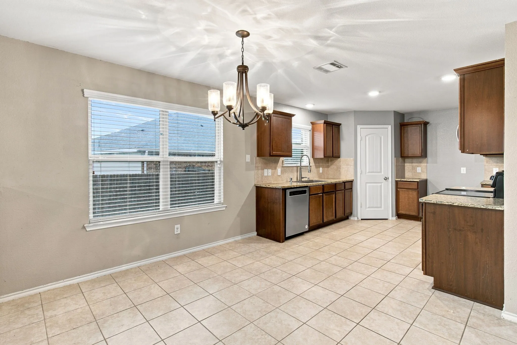 Kitchen featuring tiled flooring, wood-finish cabinetry, stone countertops, and a stainless steel dishwasher