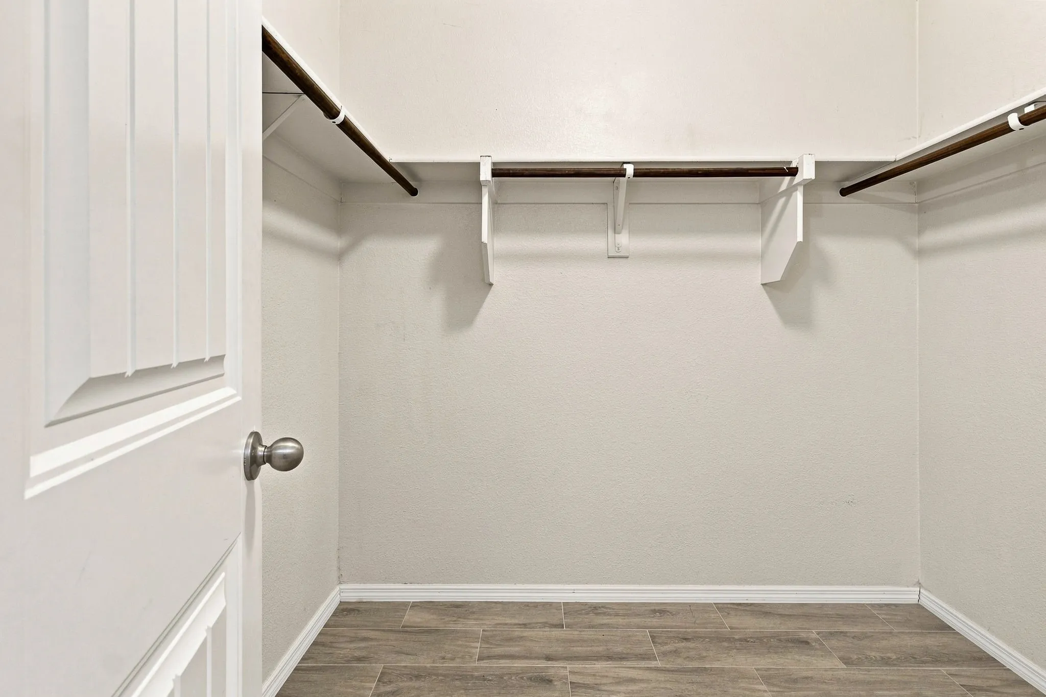 Spacious closet with wood-finish flooring, two hanging rods, and a white paneled door