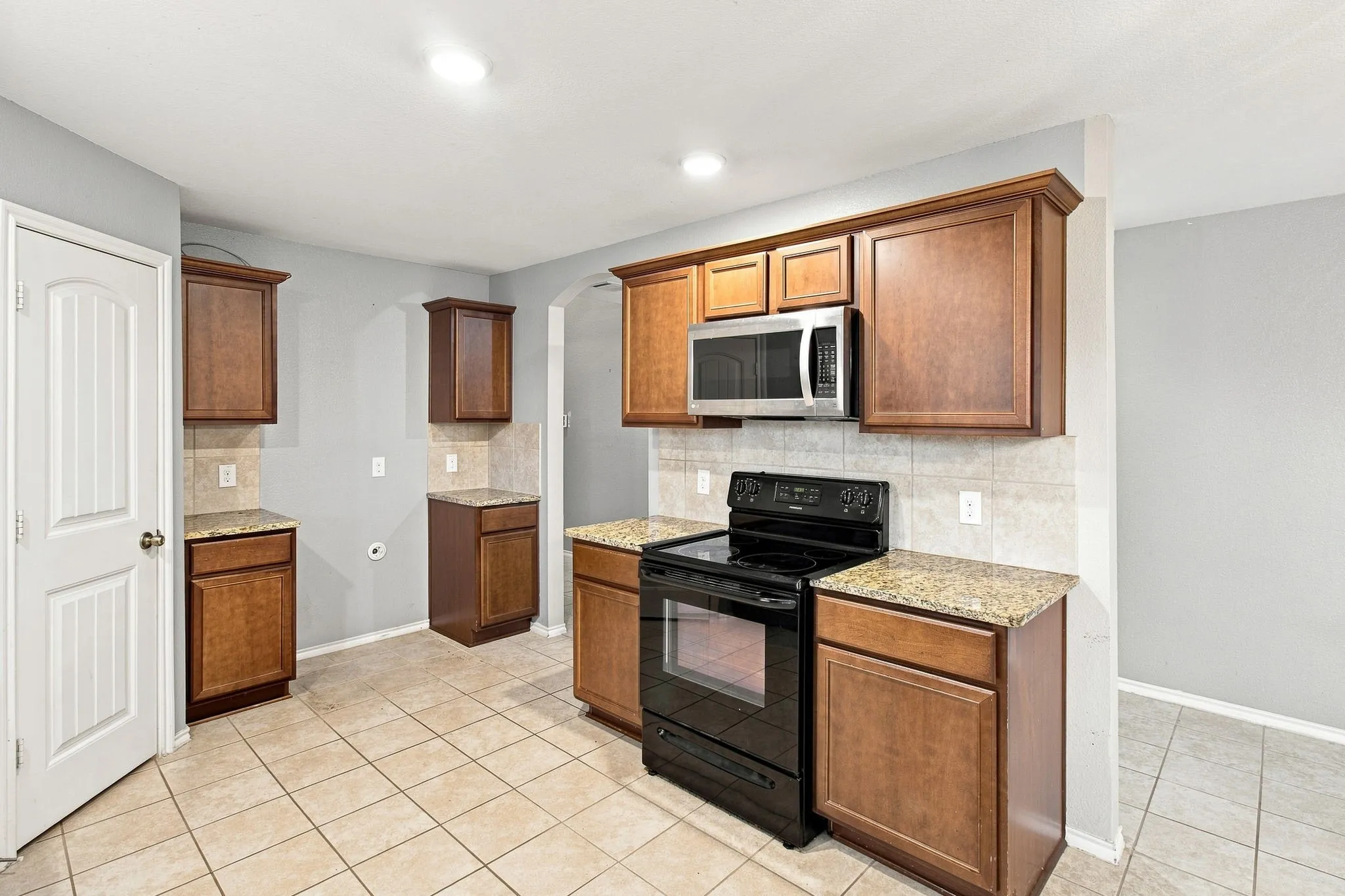 Kitchen featuring wood cabinetry, solid surface countertops, tile backsplash, built-in microwave, and a black range