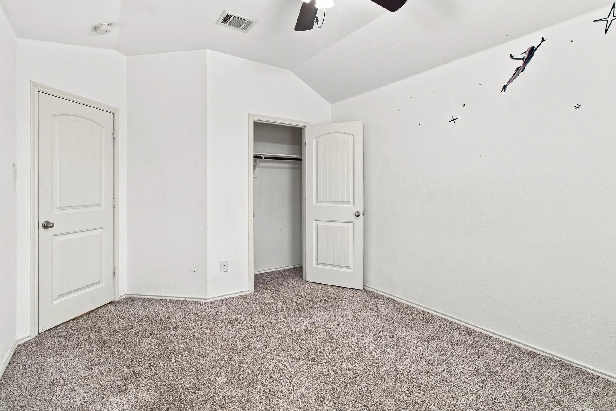 Neutral carpet flooring, vaulted ceiling, white walls, built-in closet with hanging rod, and a ceiling fan with integrated lighting