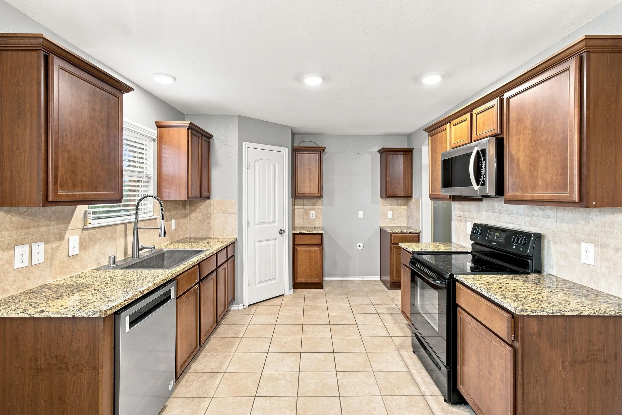 Kitchen featuring wood cabinetry, light-toned tile flooring, light-toned countertops, and stainless-steel appliances