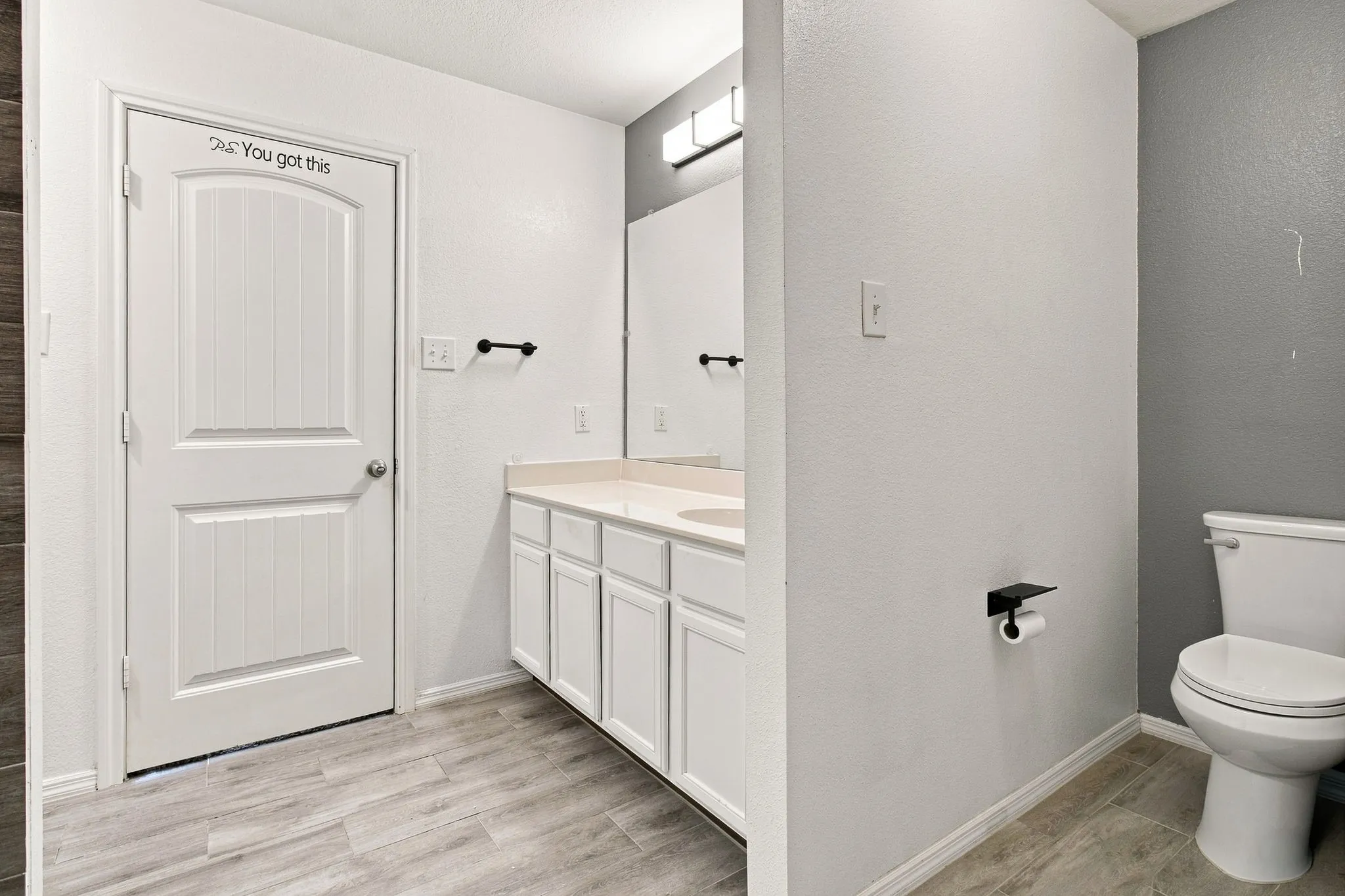 White paneled door, wood-finish flooring, vanity with white cabinetry, light countertop, and a built-in toilet