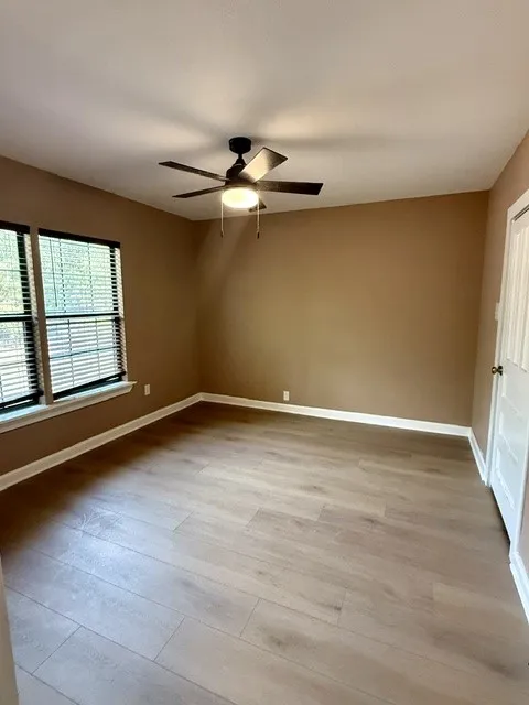 Recessed window with horizontal blinds, wood-finish flooring, ceiling fan with integrated lighting, and a paneled door