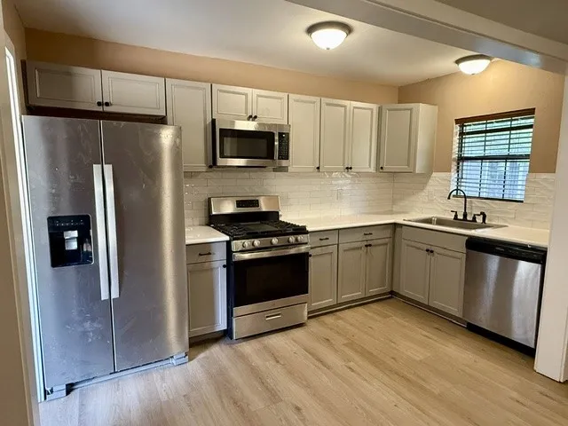Kitchen featuring stainless steel appliances, light gray cabinetry, white countertops, subway tile backsplash, and wood-finish flooring