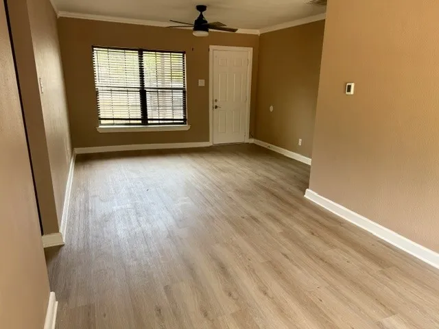 Wood-finish flooring throughout, ceiling fan with integrated lighting, and crown molding accents