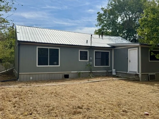 Gray horizontal siding with white trim, a metal roof, and a white entry door