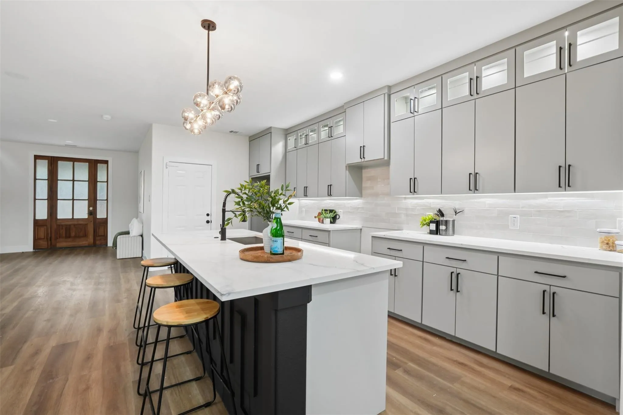 Kitchen with wood-finish flooring, an expansive island featuring a quartz countertop, a modern pendant light fixture, and extensive light gray cabinetry