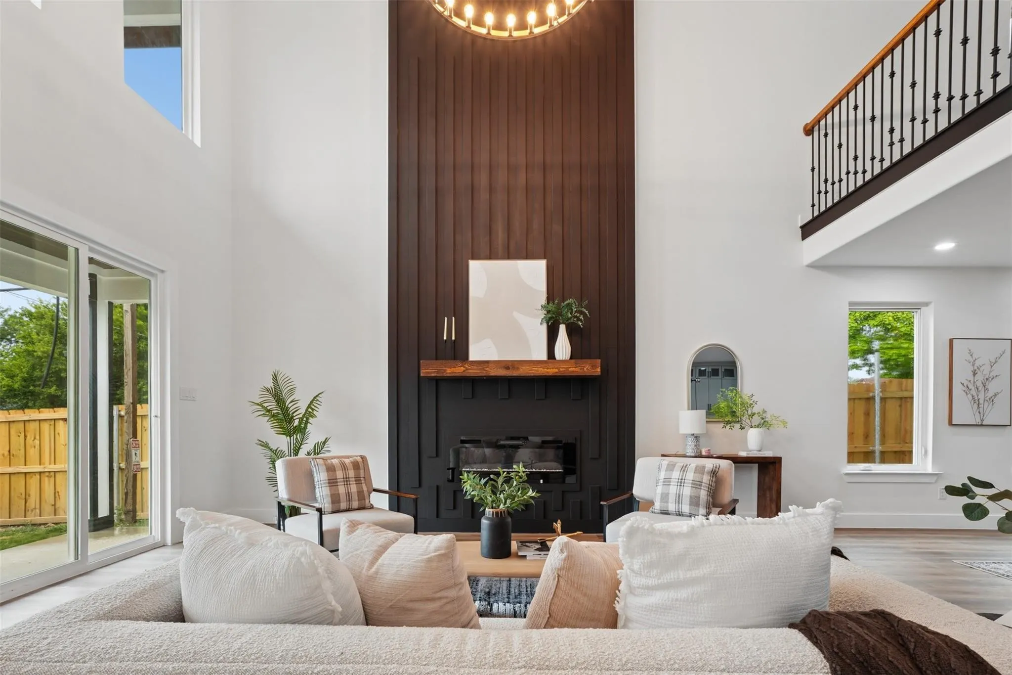 Two-story living area featuring a dark wood-paneled fireplace with a substantial mantel, a wrought iron staircase, and large sliding glass doors