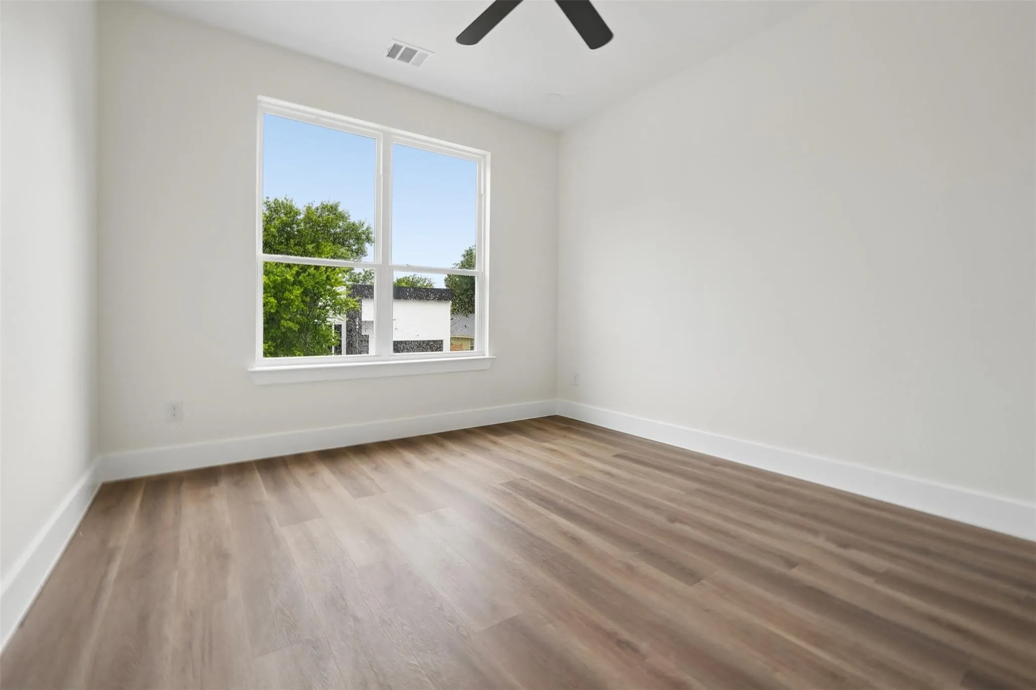 Spacious room featuring wood-finish flooring, a large window, and a ceiling fan