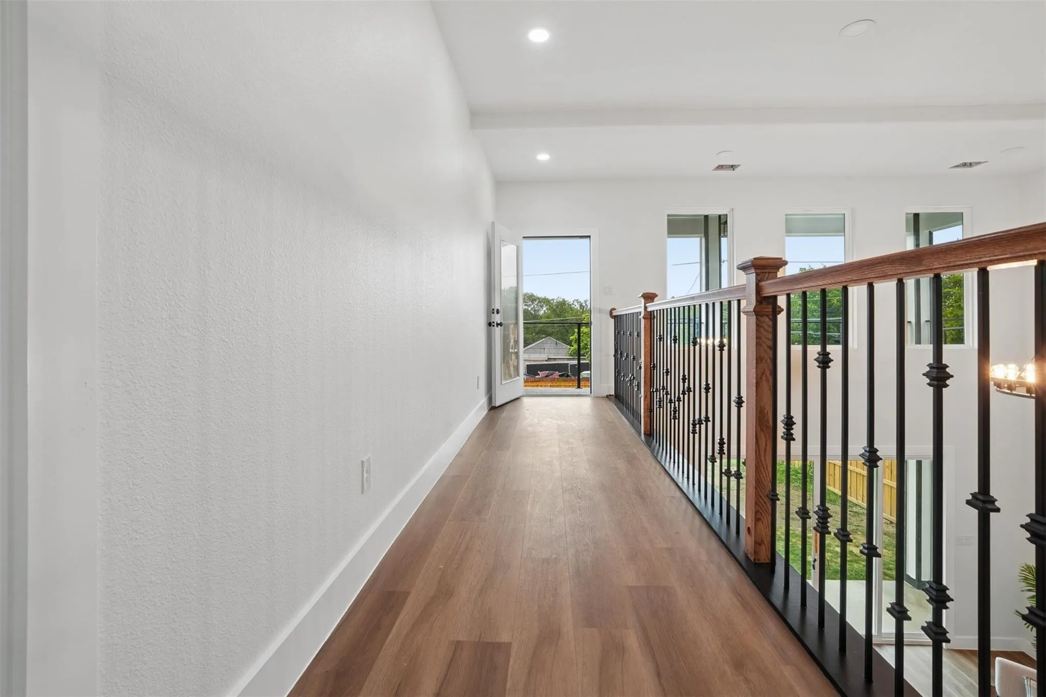 Wood-finish flooring, white walls, recessed lighting, wrought iron and wood banister, and a glass-paneled door leading to an exterior space