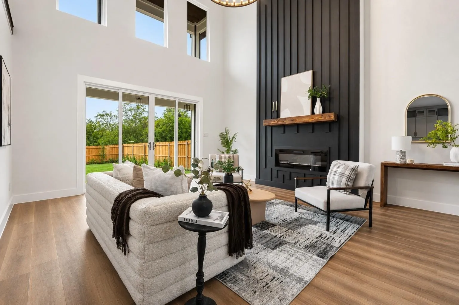 High ceilings with upper windows, a fireplace with a black slat wall and wood mantel, wood-finish flooring, and sliding glass doors opening to the backyard