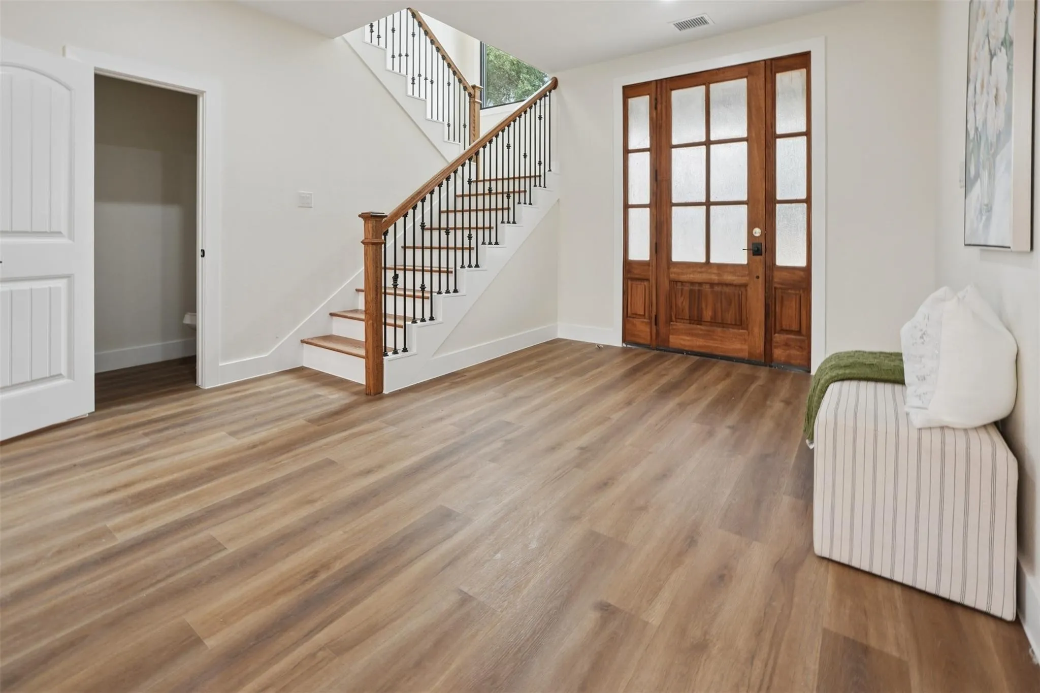 Wood-finish flooring, staircase with wood banister and wrought iron spindles, paneled entry door with frosted glass, and white walls