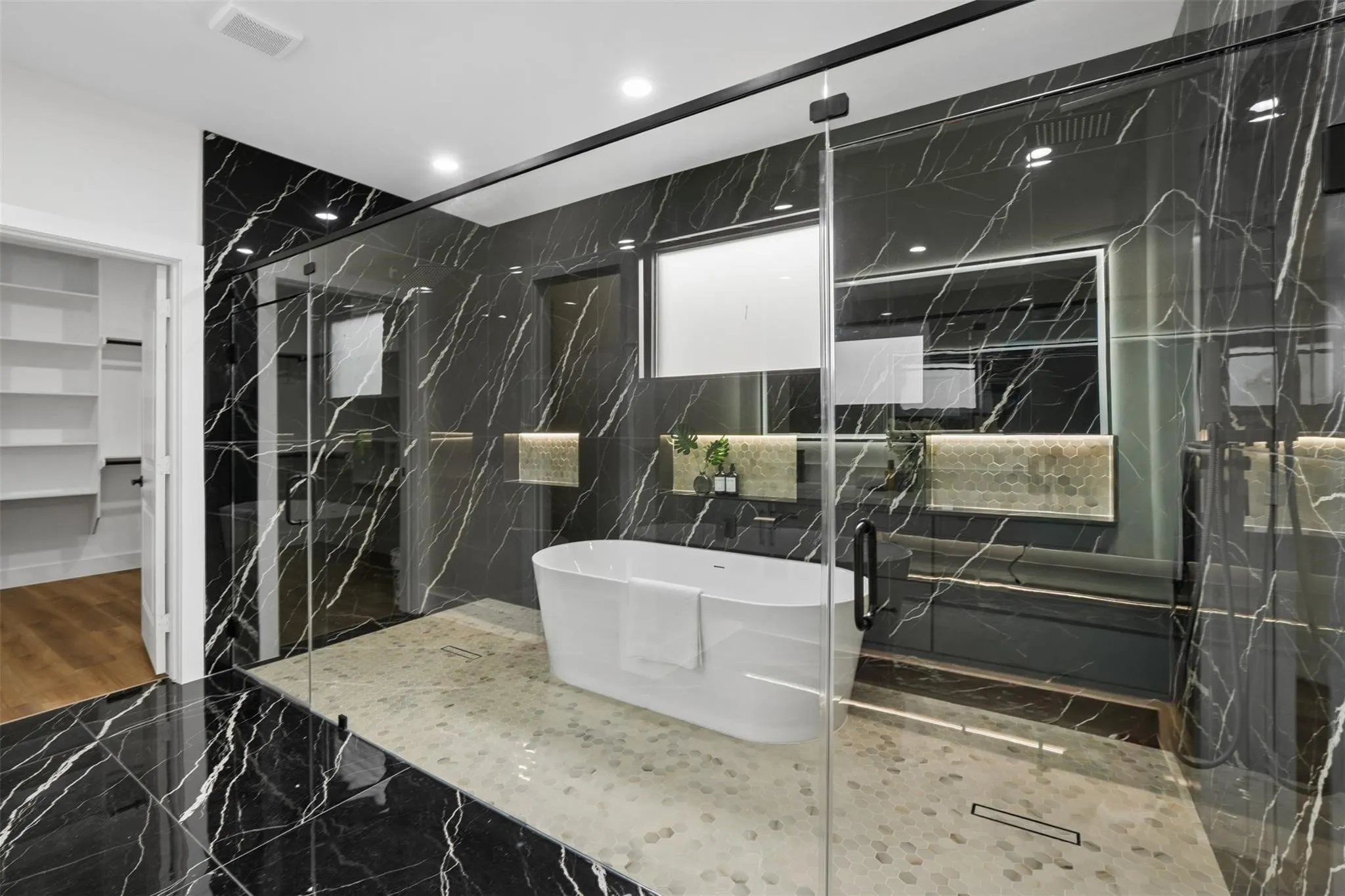 Glass-enclosed wet room featuring a freestanding soaking tub, black marble-look wall and floor tile, and a pebble-finish shower floor