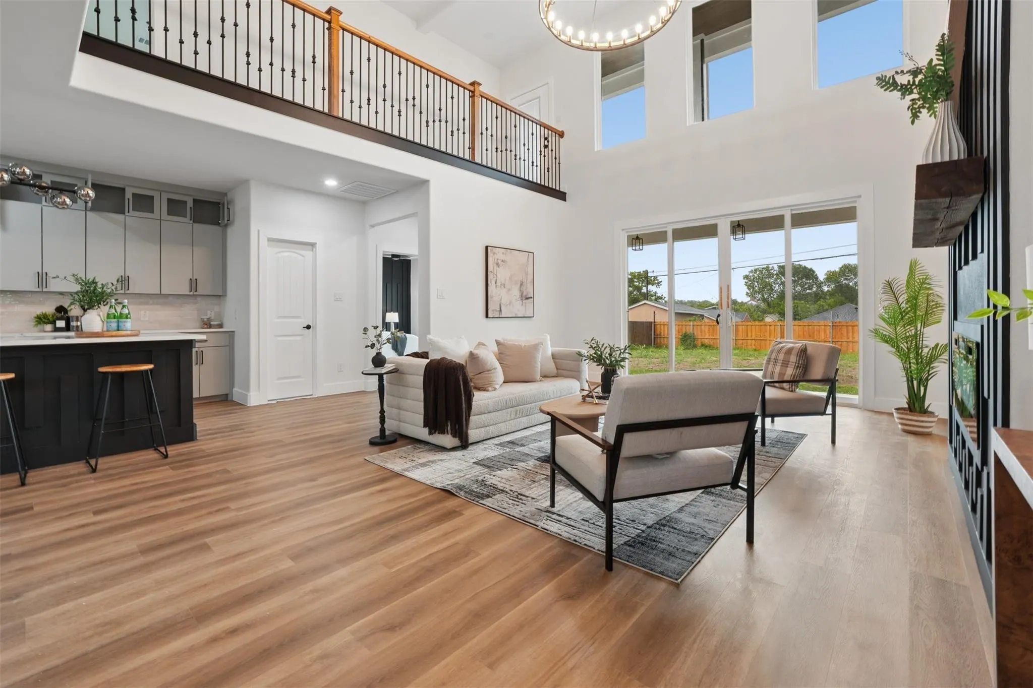 Open-concept living area featuring wood-finish flooring, a kitchen island with seating, a second-story interior balcony, and large sliding glass doors