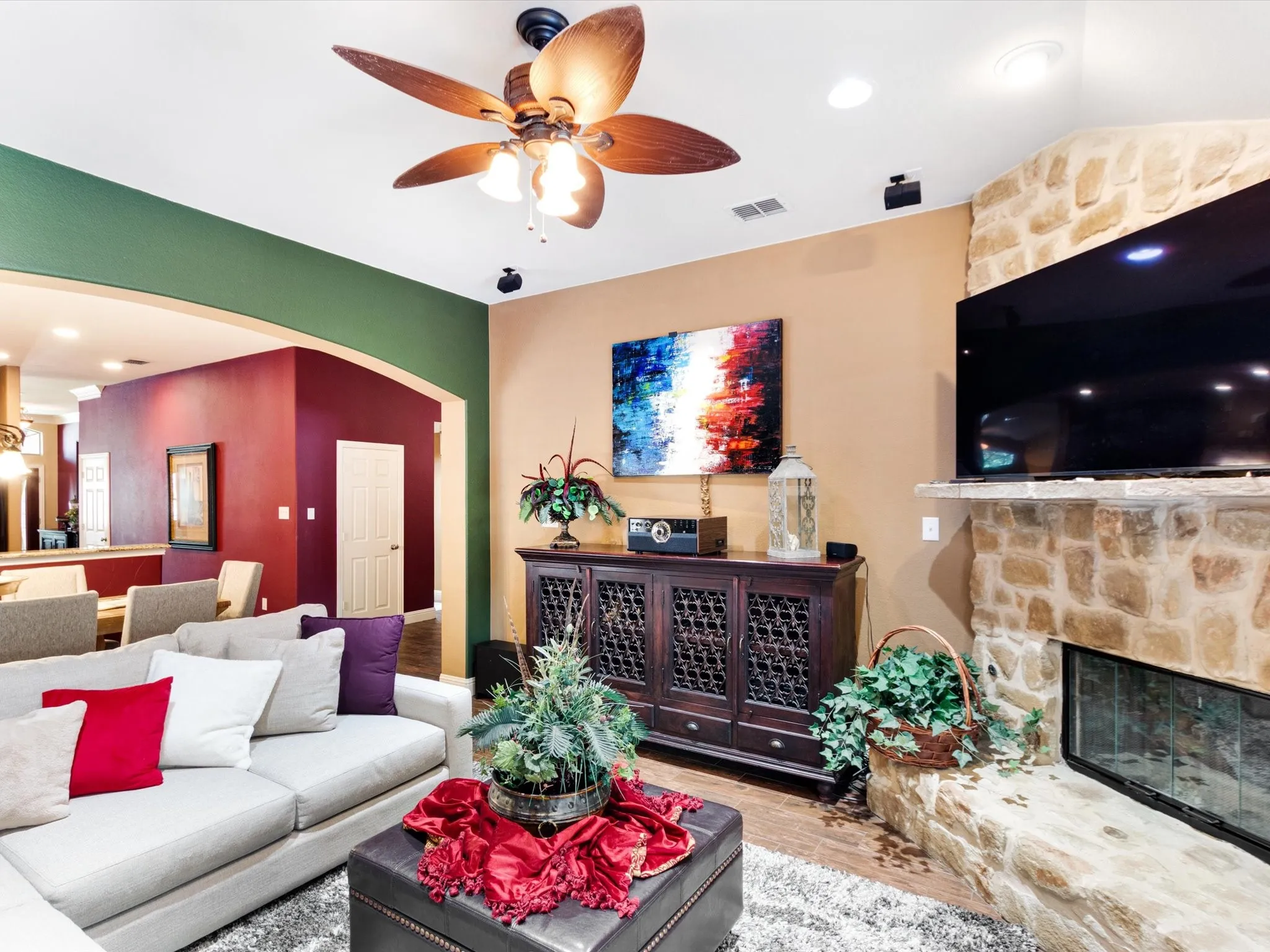 Stone-faced fireplace with hearth, wood-finish flooring, ceiling fan, and recessed lighting