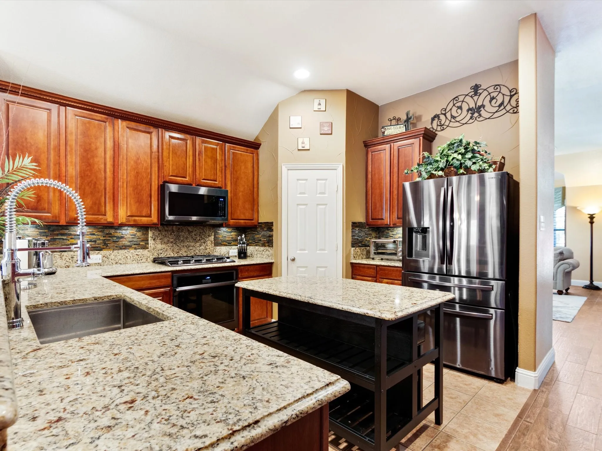 Kitchen featuring wood cabinetry, stainless steel appliances, speckled countertops, a tile backsplash, and a central island