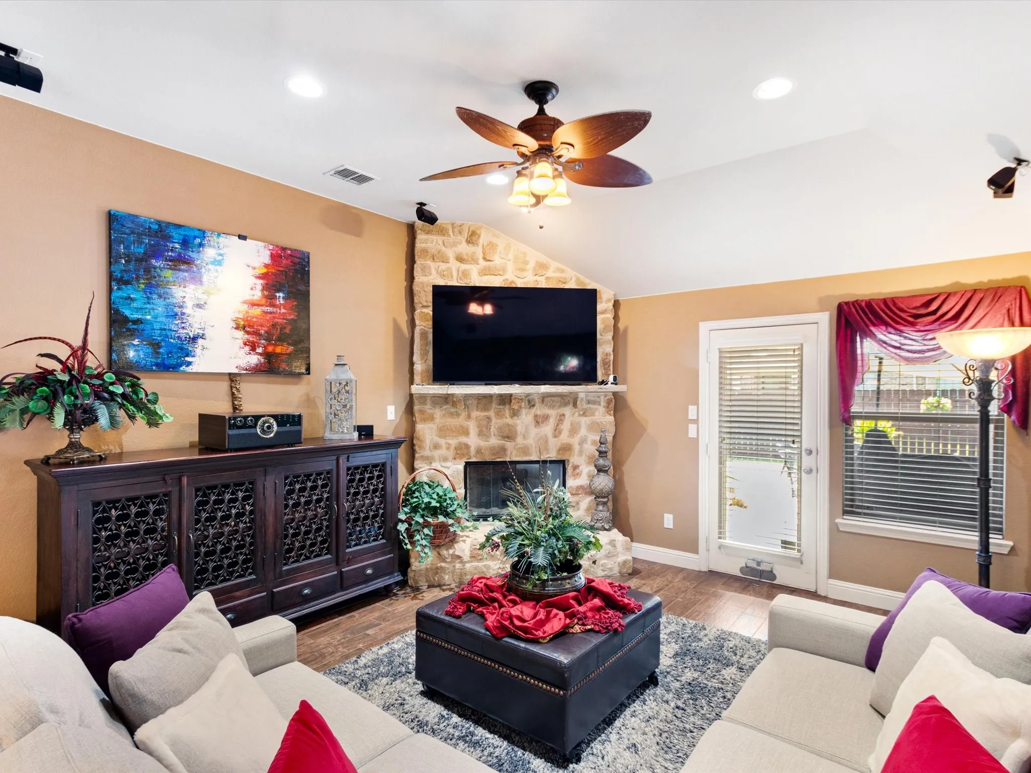 Vaulted ceiling, stone-clad fireplace, wood-finish flooring, recessed lighting, and a ceiling fan with light fixture