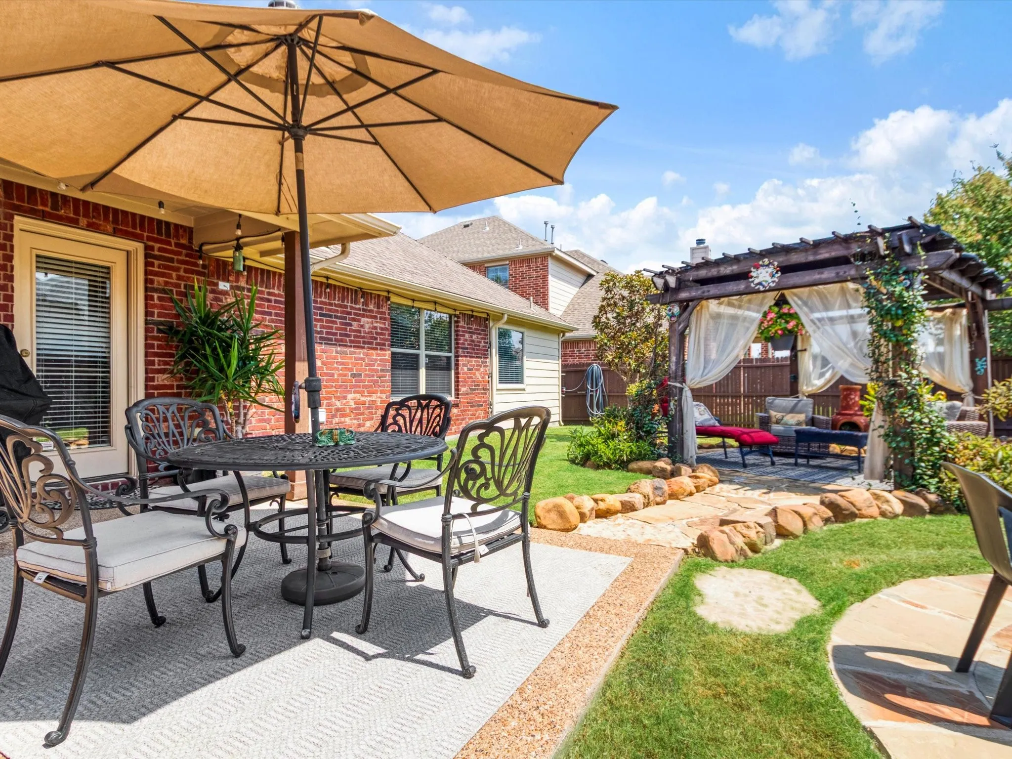 Outdoor living area featuring a pergola with drapery, a stone pathway, a manicured lawn, and brick exterior